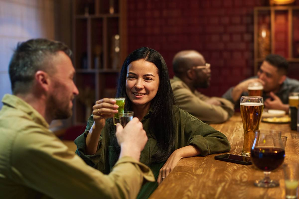 Friends raising glasses at a bar, one laughing towards the camera
