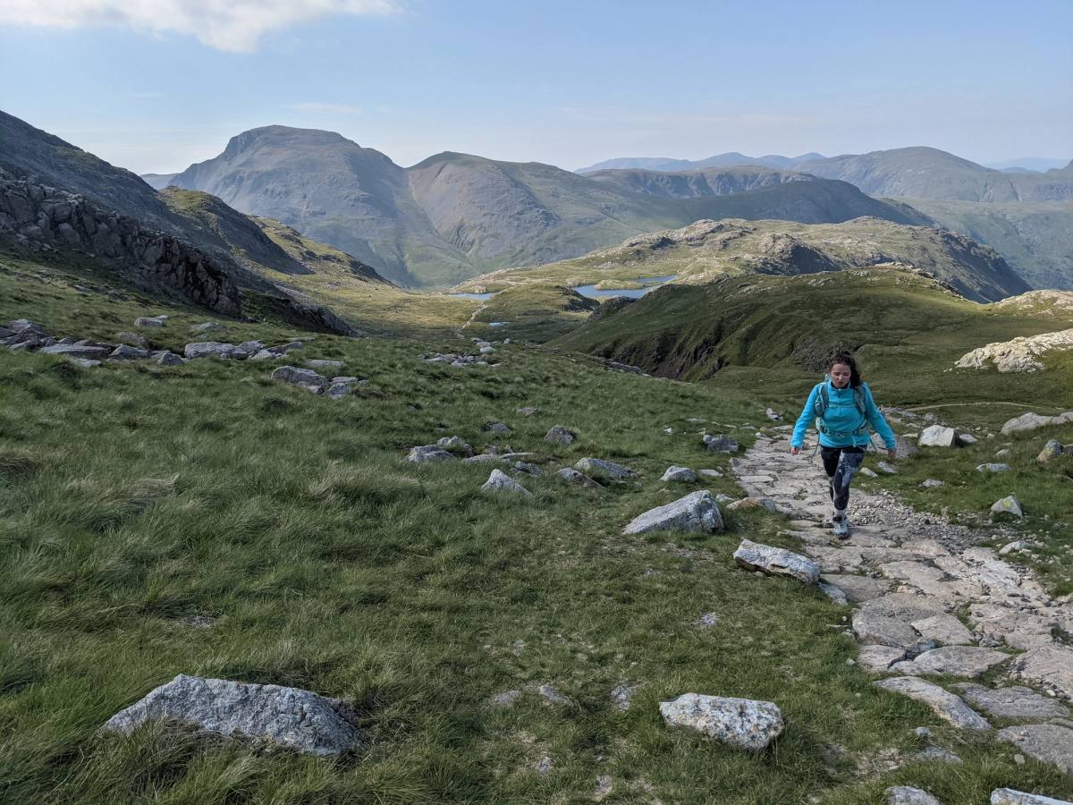 person walking up a paved path on the corridor route up scafell pike lush green and mountains in the background