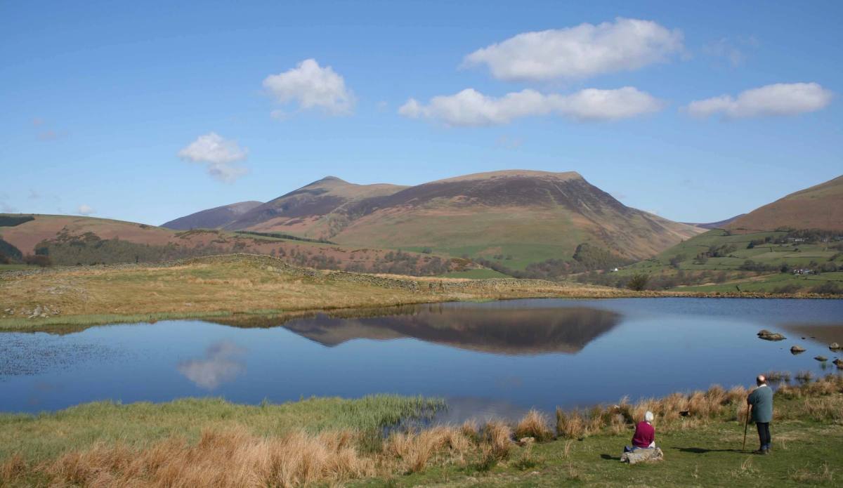 A tarn lying in green hedged fields with the fells rising beyond