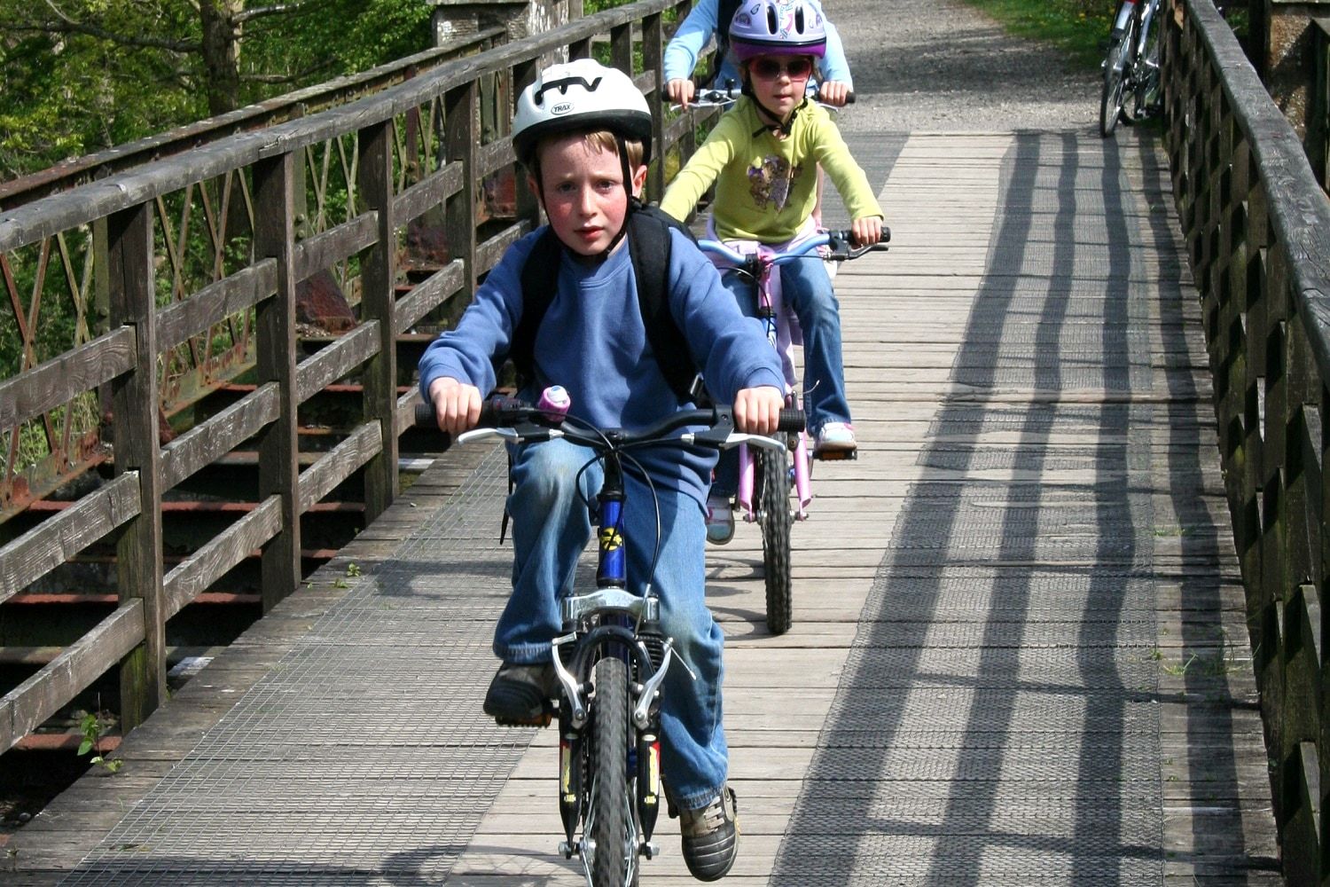 Children riding bikes along a raised timber boardwalk through the trees