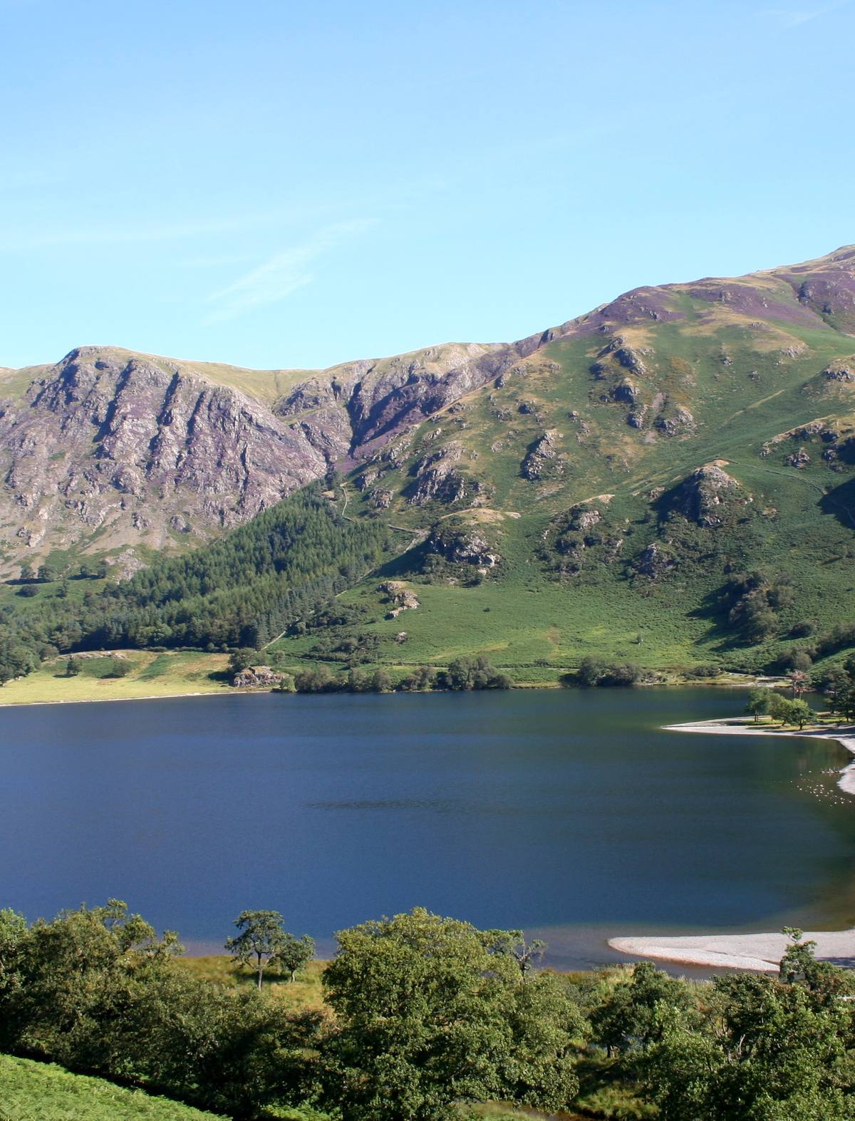 A shingle beach curving into the lake below steep bracken-covered fells