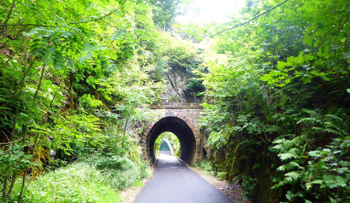 The path running through an old stone railway tunnel into green light beyond