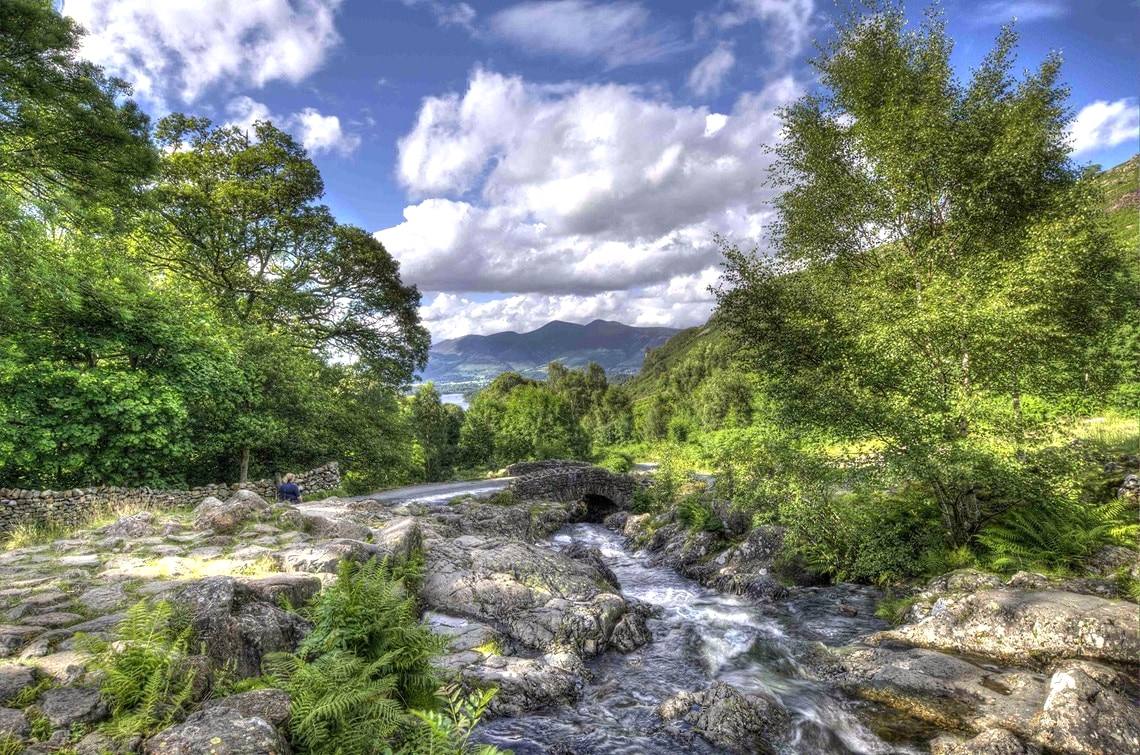 A beck running over rocks below Ashness Bridge with Derwentwater beyond