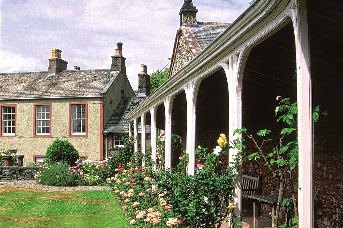 A country house behind a rose garden with a long pillared veranda