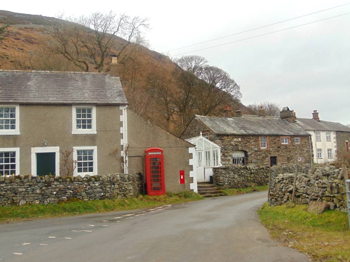A red telephone box beside stone village houses on a quiet road