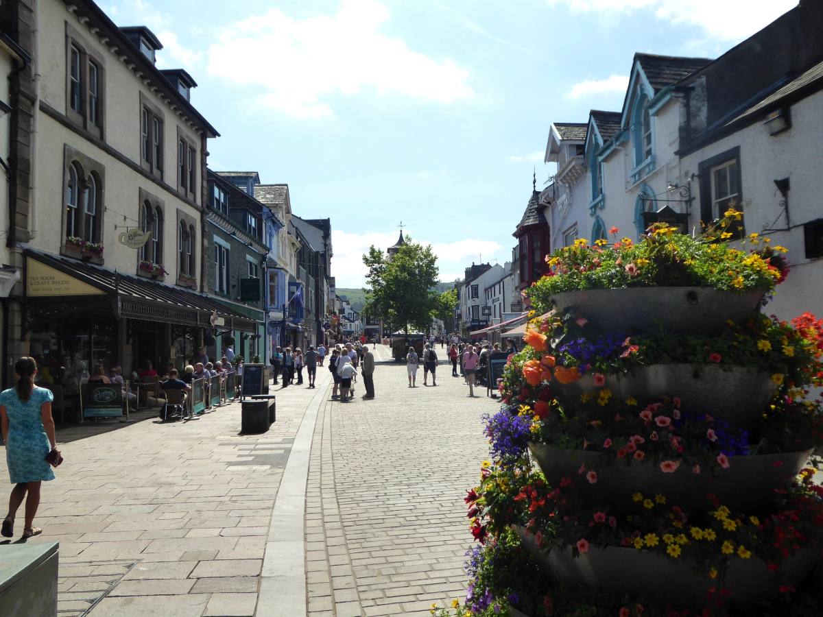 Shoppers along Keswick main street between hanging baskets and flower planters