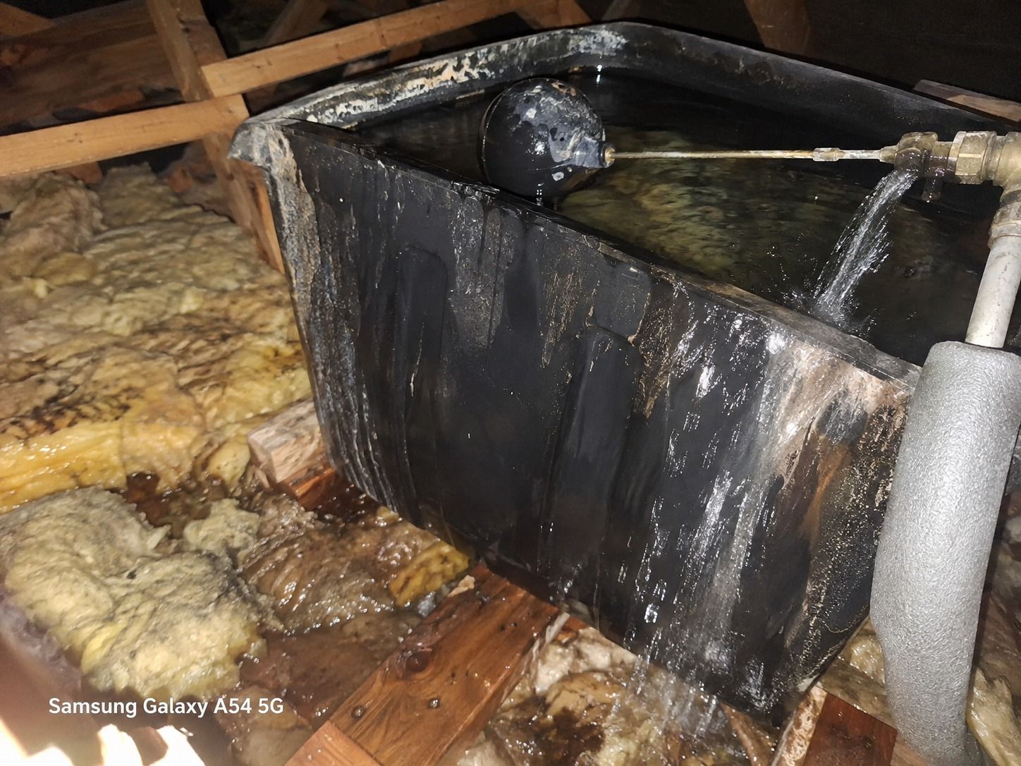 Loft cold water tank with a faulty float valve overflowing onto damp insulation below