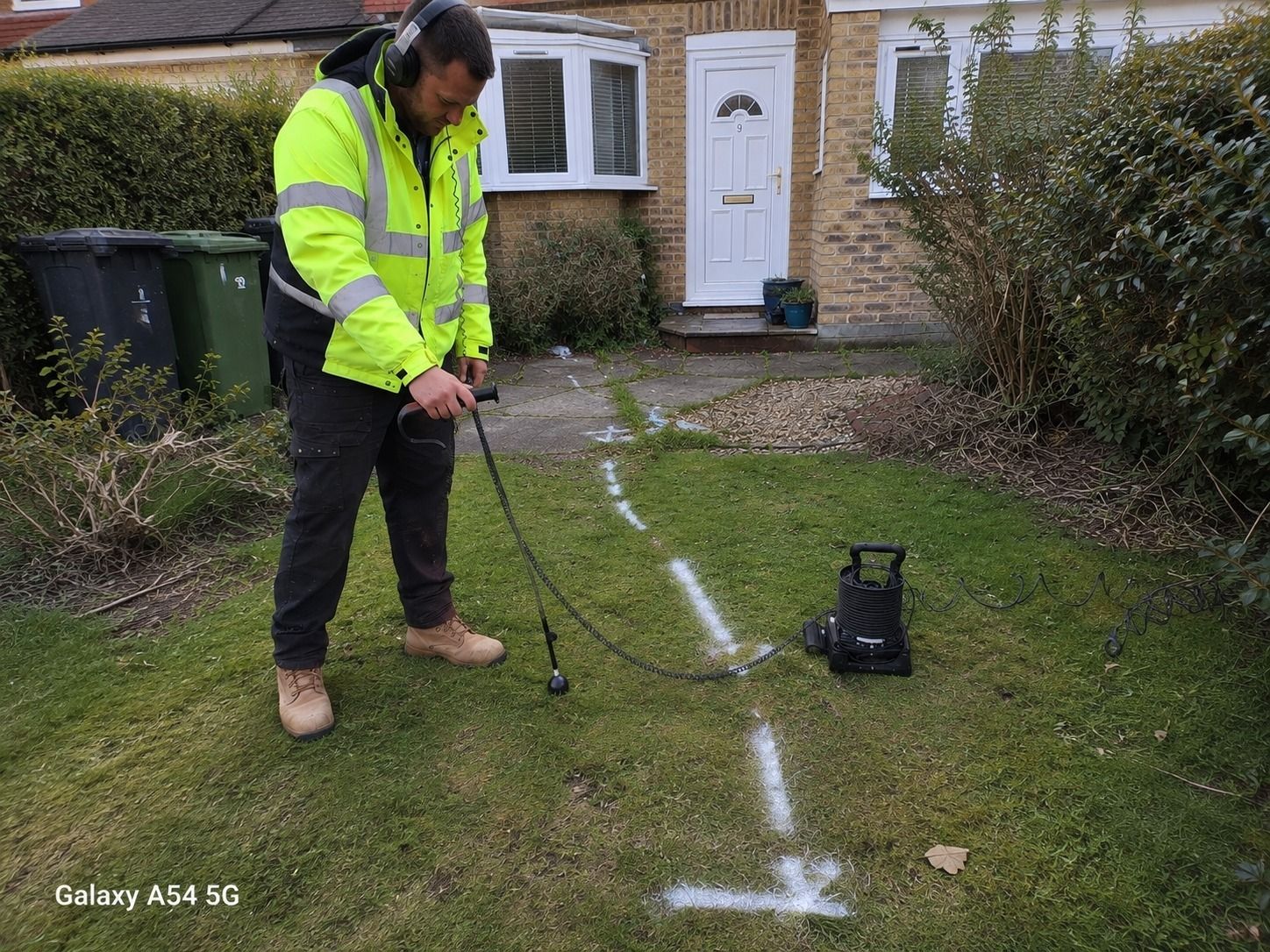 Engineer using acoustic ground microphone to trace a mains supply pipe leak beneath a front garden in Croydon