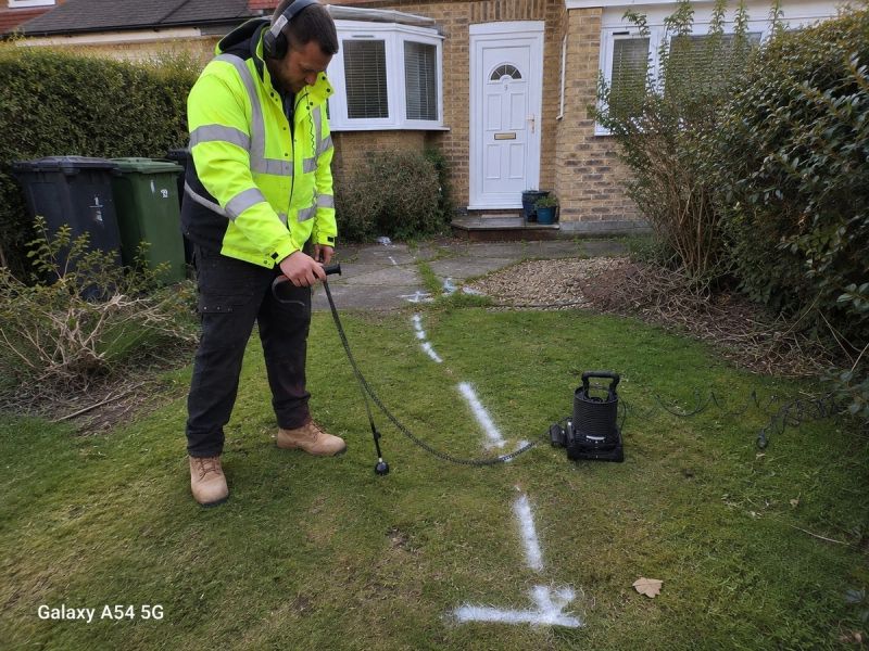 Engineer using acoustic ground microphone to trace a mains supply pipe leak beneath a front garden in Croydon