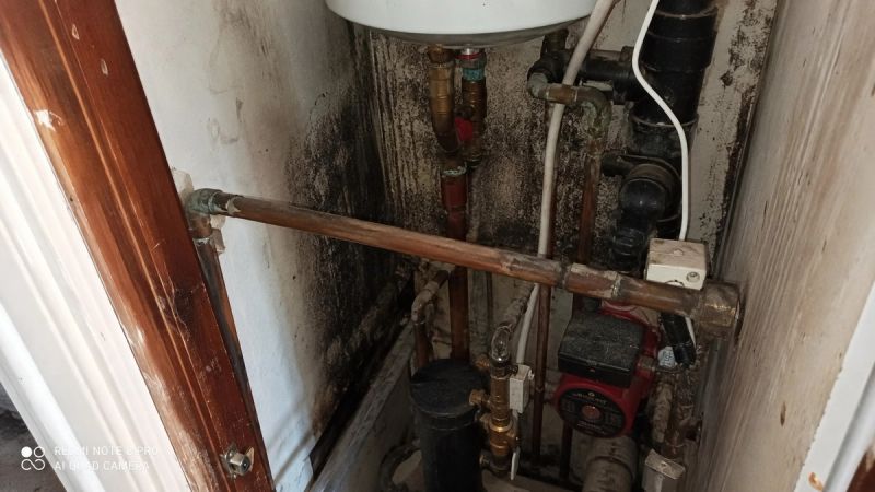 Damp, stained pipework in a UK boiler cupboard showing signs of a hidden water leak