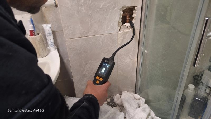 Engineer using a trace gas detector on a bathroom tile wall to locate a hidden pipe leak in a Bromley flat
