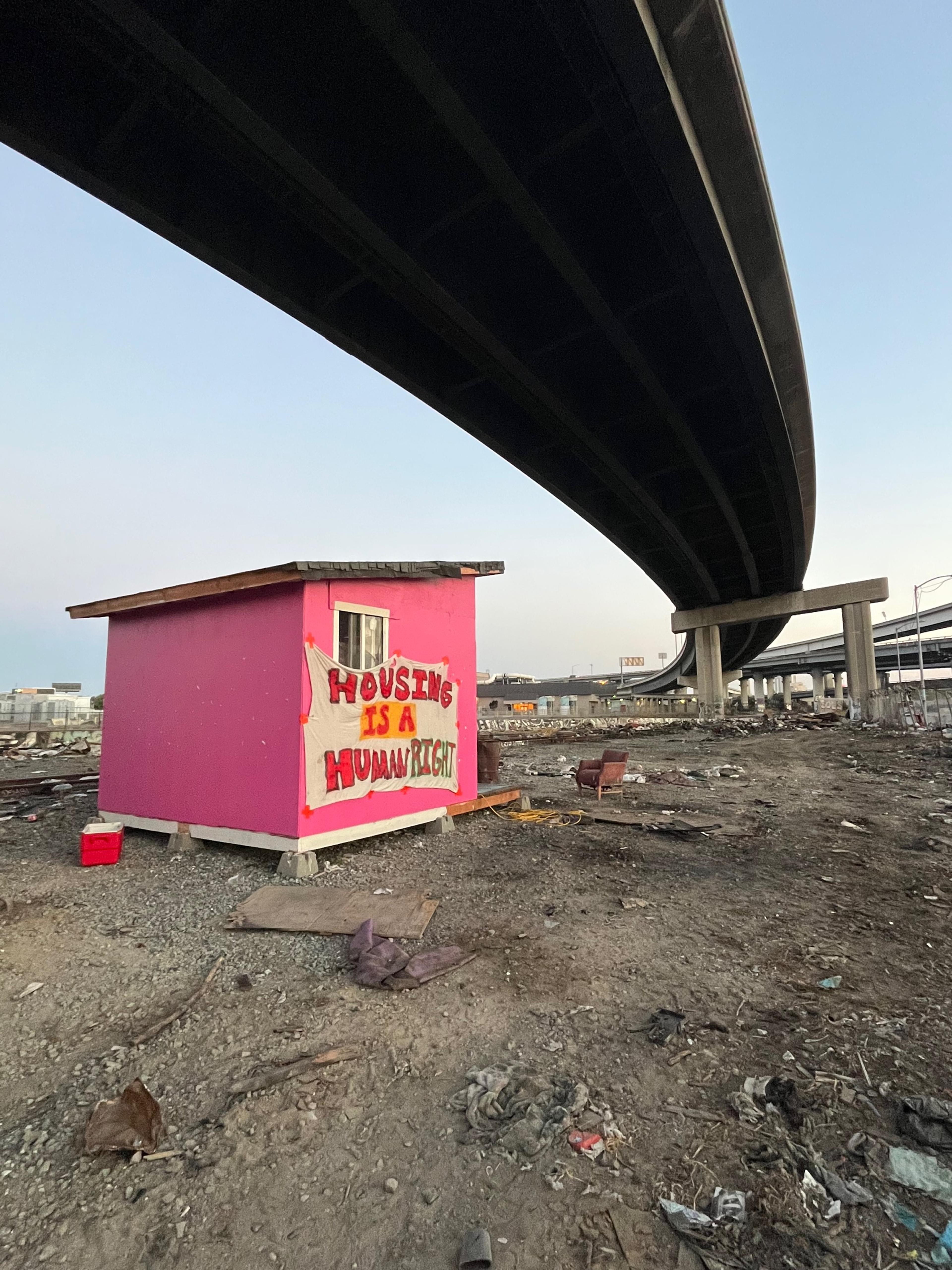 A shack with the slogan 'Housing is a human right' painted on it sits under a bridge