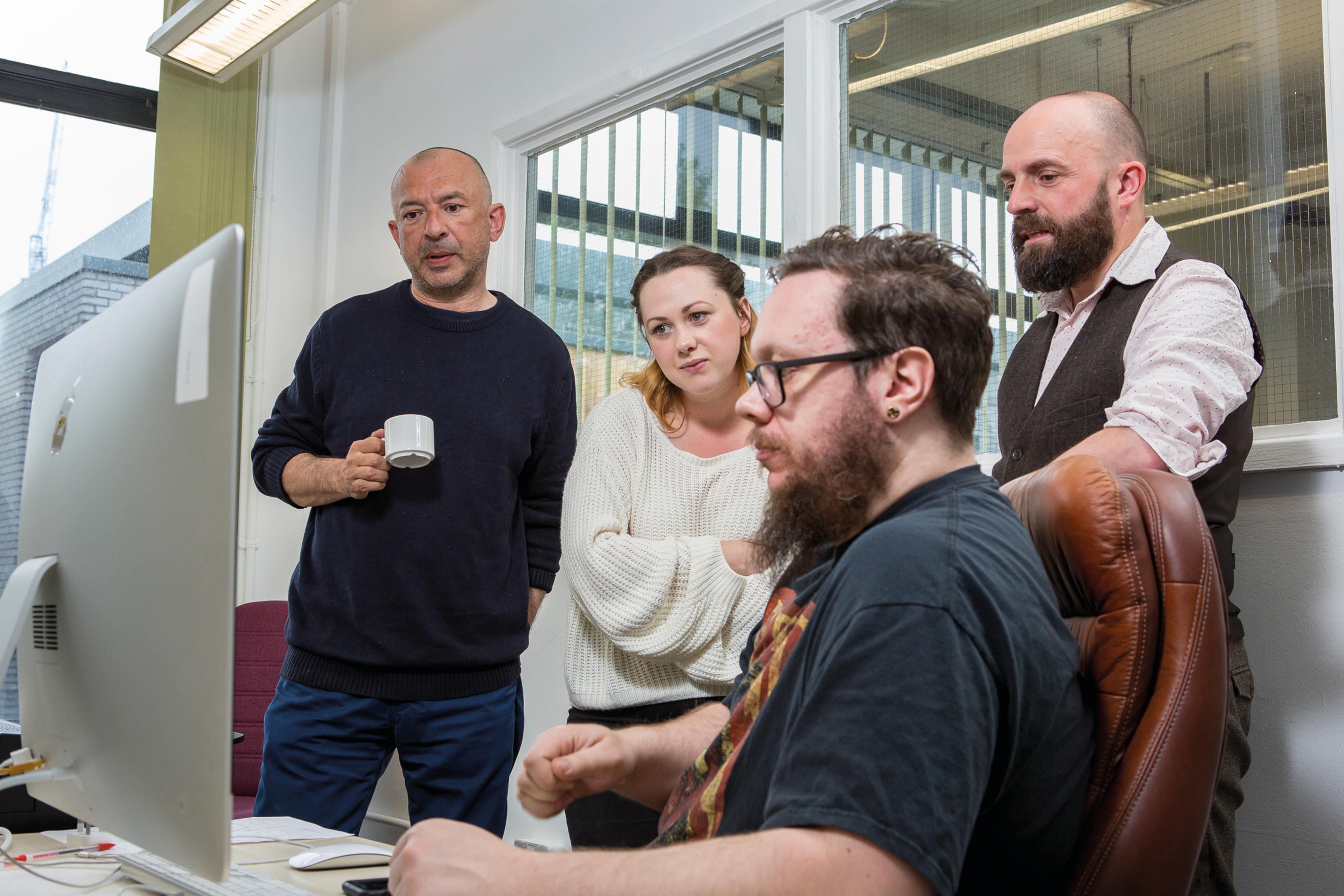 (Left to right): Big Issue North editorial staff Kevin Gopal, deputy editor Antonia Charlesworth, producer Christian Lisseman and designer Mark Wheeler all stand looking at a computer screen.