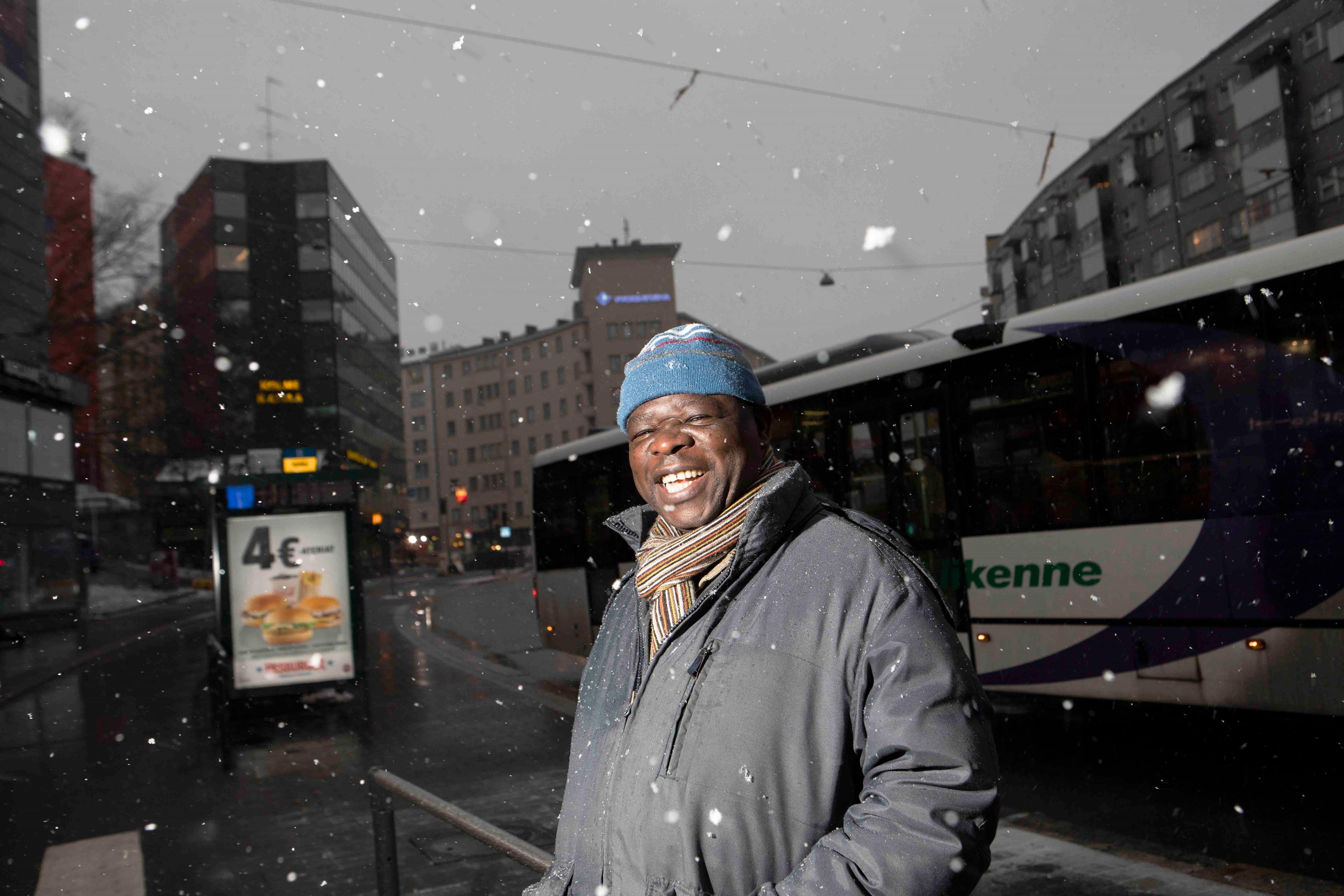 A man smiles in the snow in front of a bus