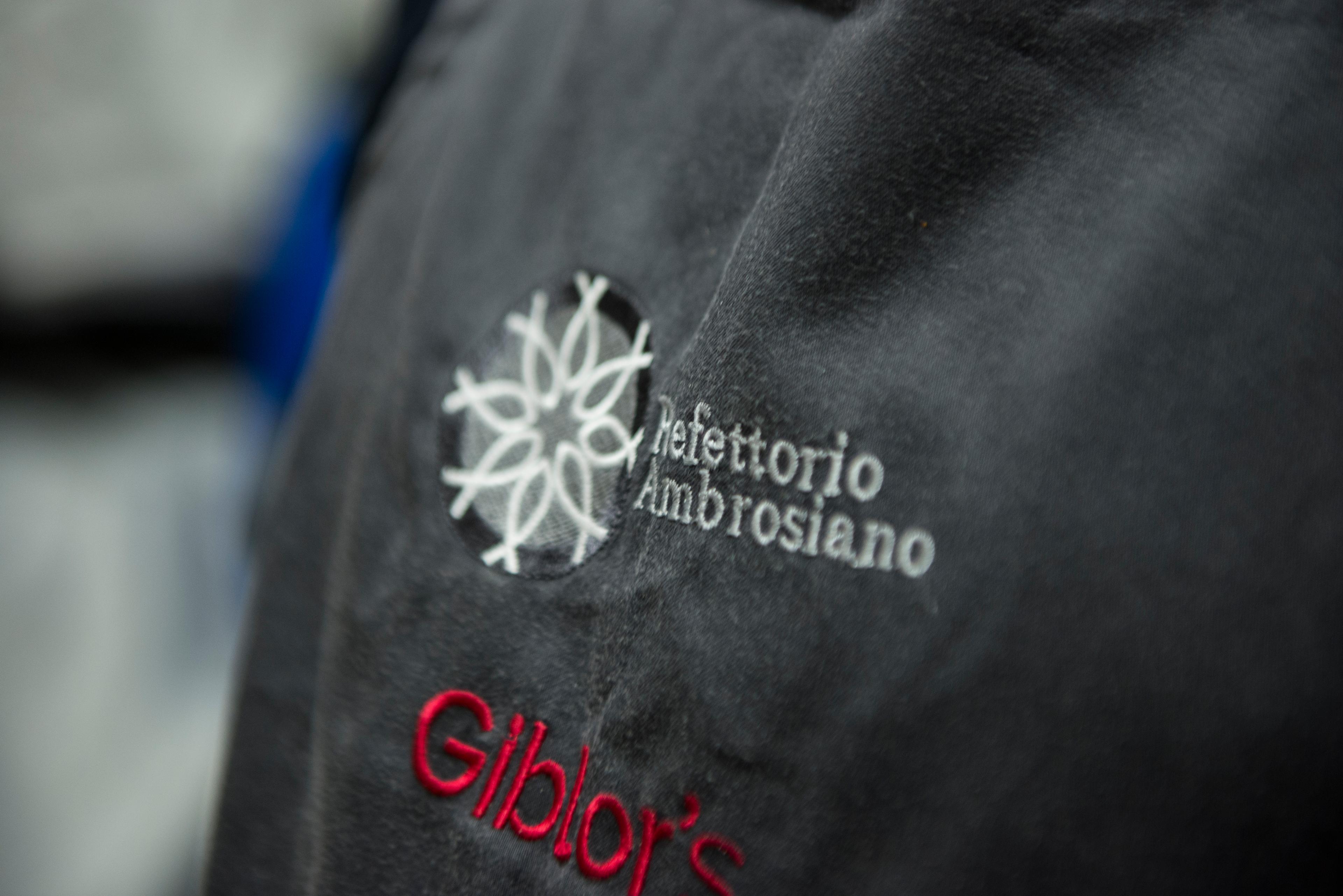 Refettorio Ambrosiano logo on a chef's overalls.