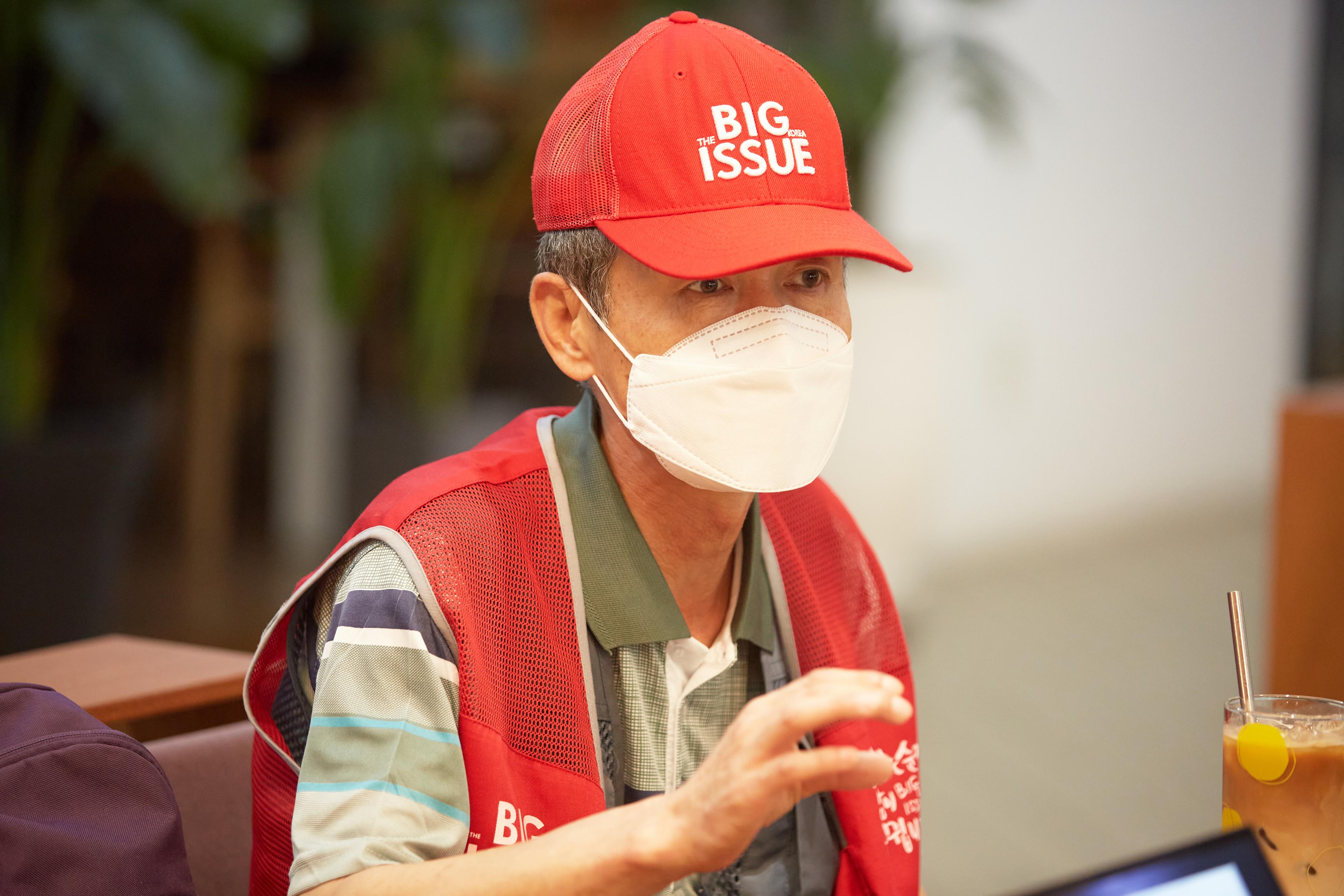 A man in a red hat and white masks talks to an interviewer