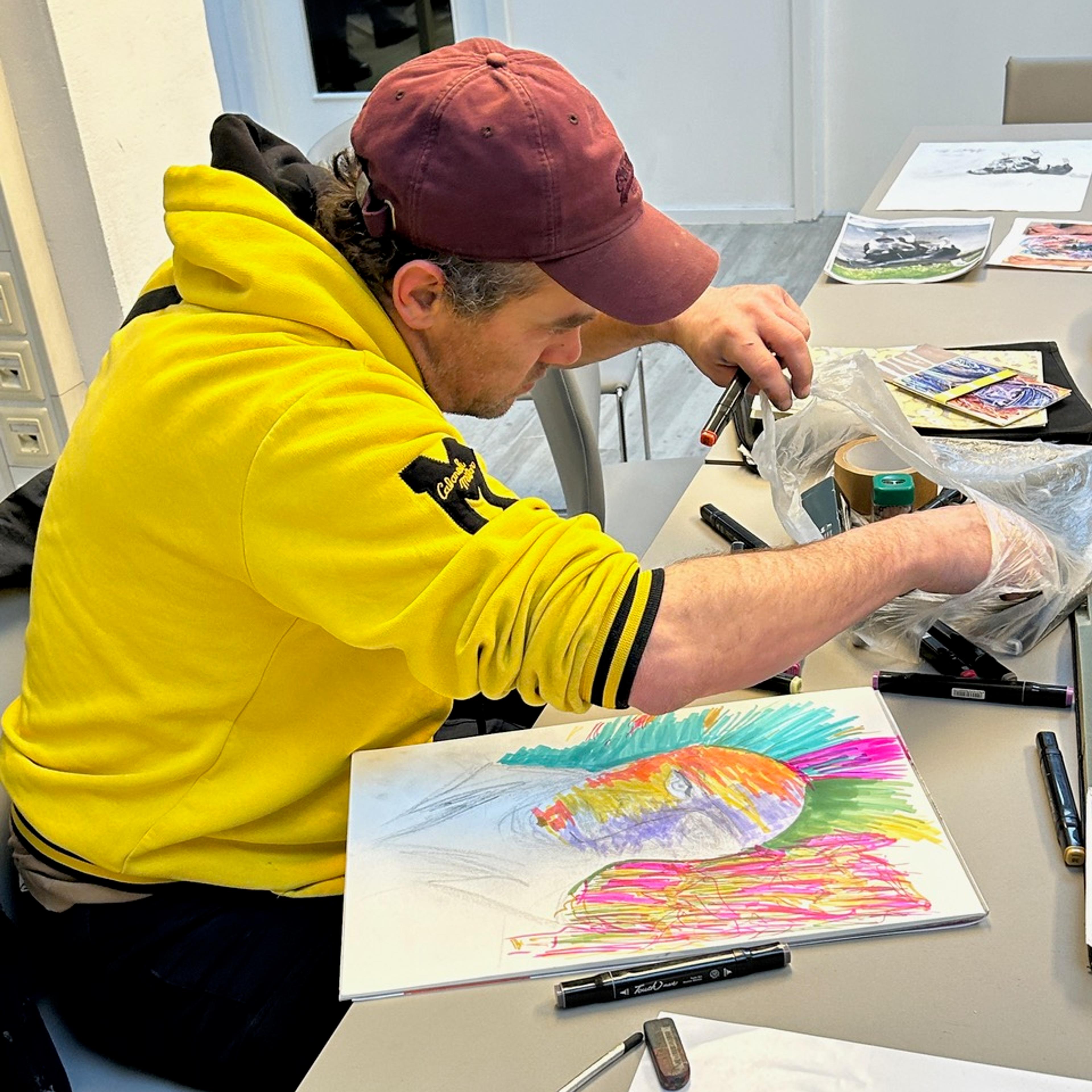 a man in a yellow hoodie sitting at a table, drawing