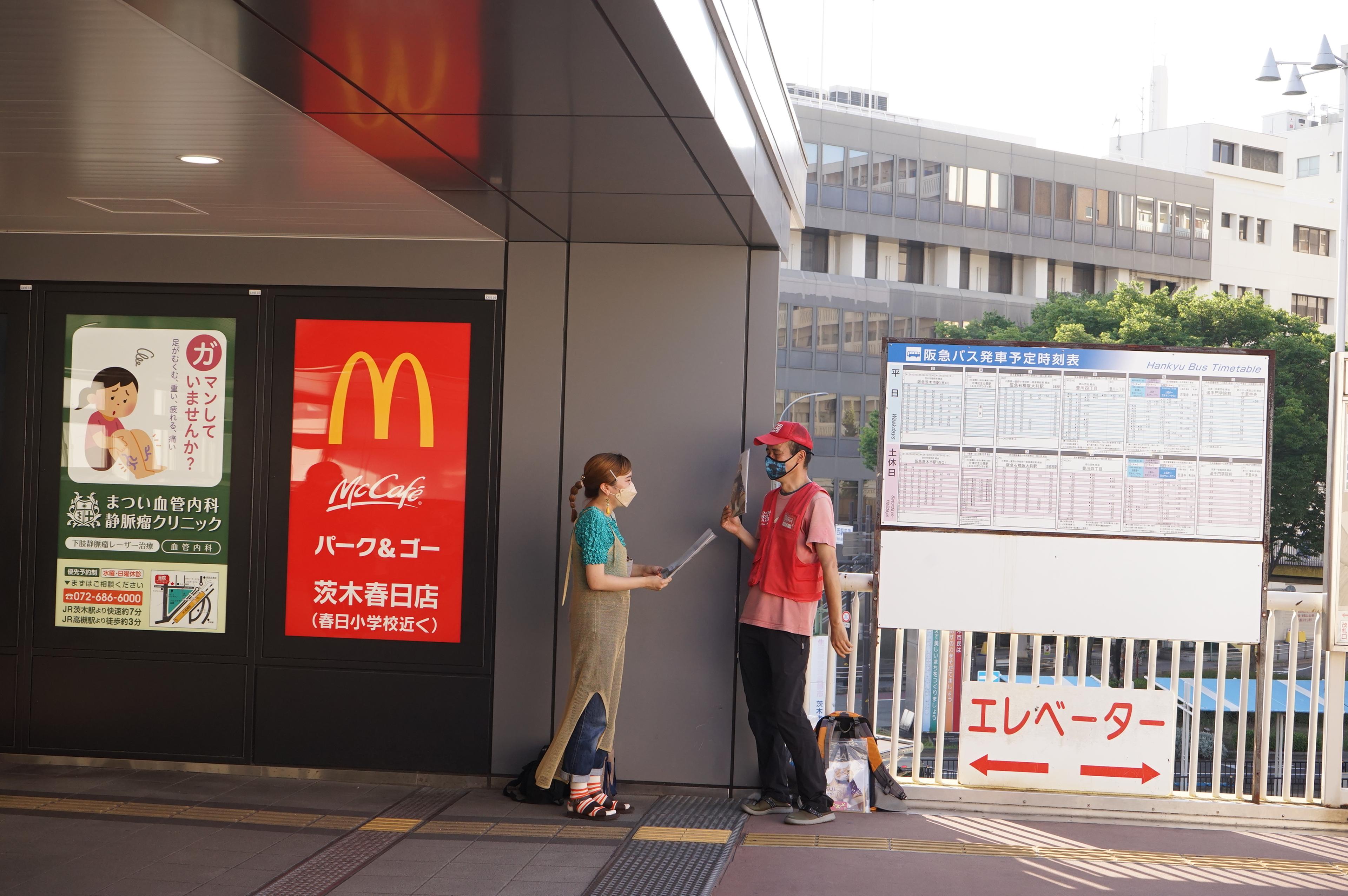 A man sells a street paper to a woman next to a train station entrance