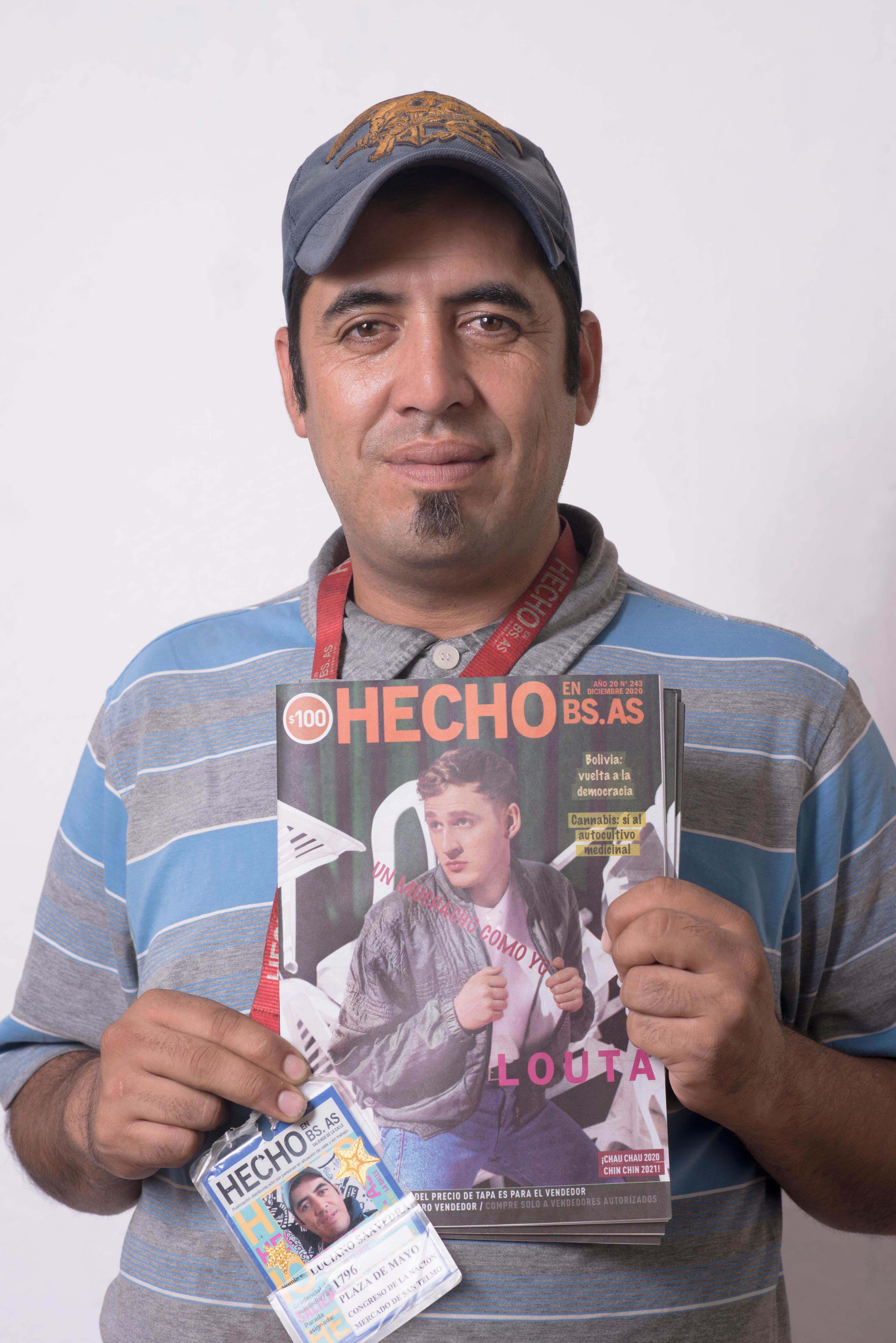 Hecho vendor Luciano is wearing a blue cap and stripy polo top and is holding a copy of the Hecho en Bs. As. street paper