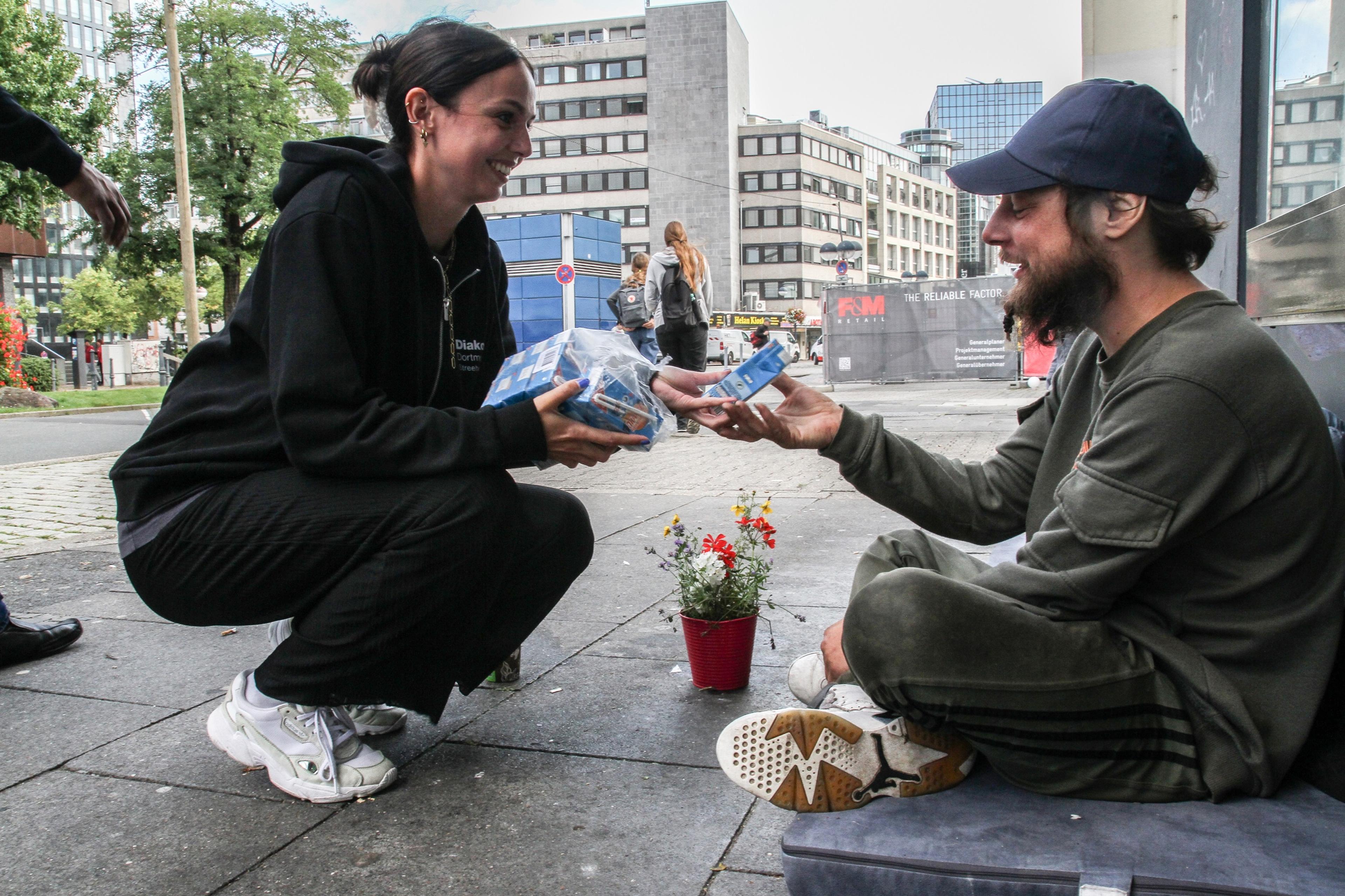 a woman hands a bearded man a carton of juice