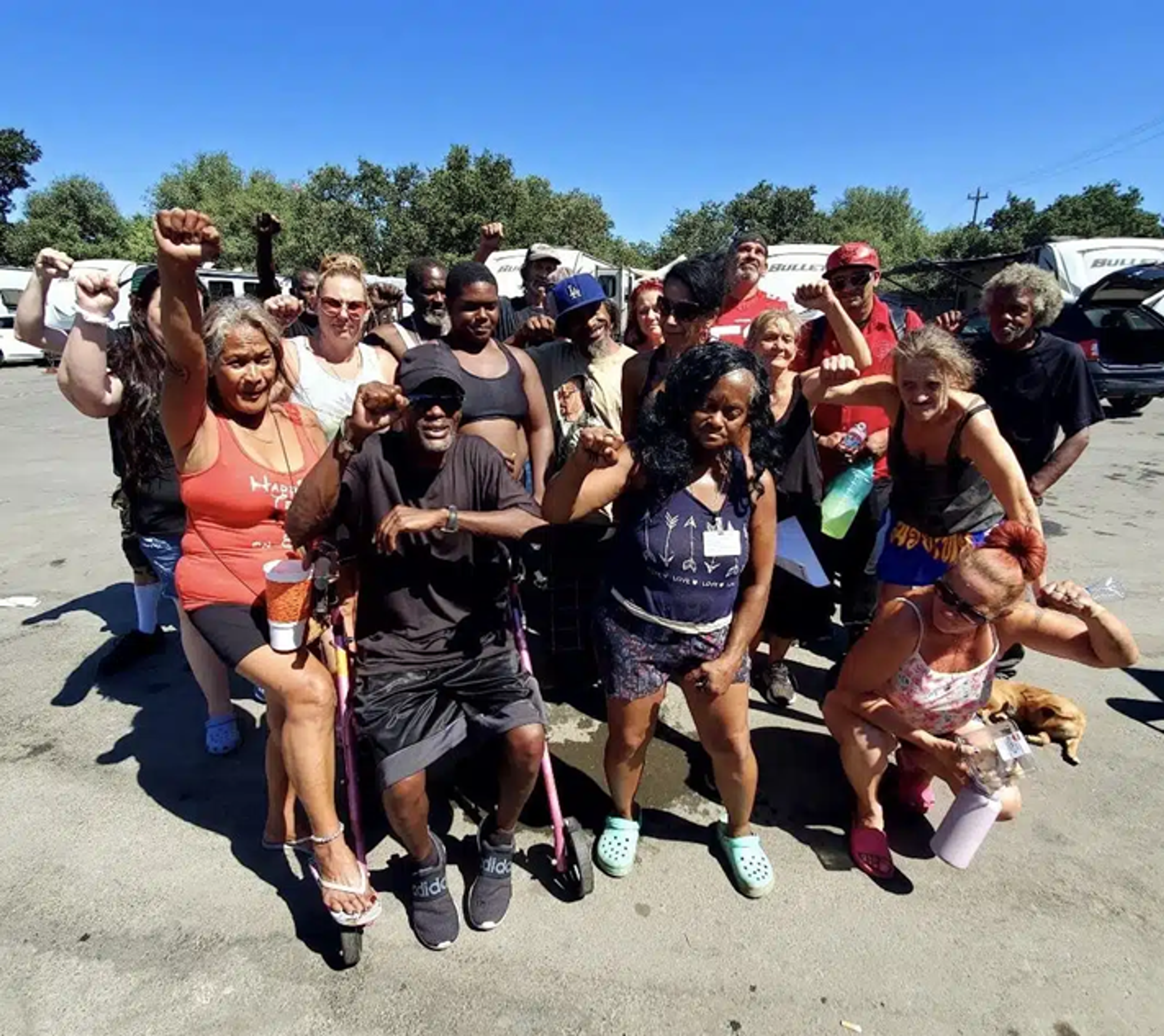 a group of people facing the camera with a campsite in the background, all with their fists in the air.