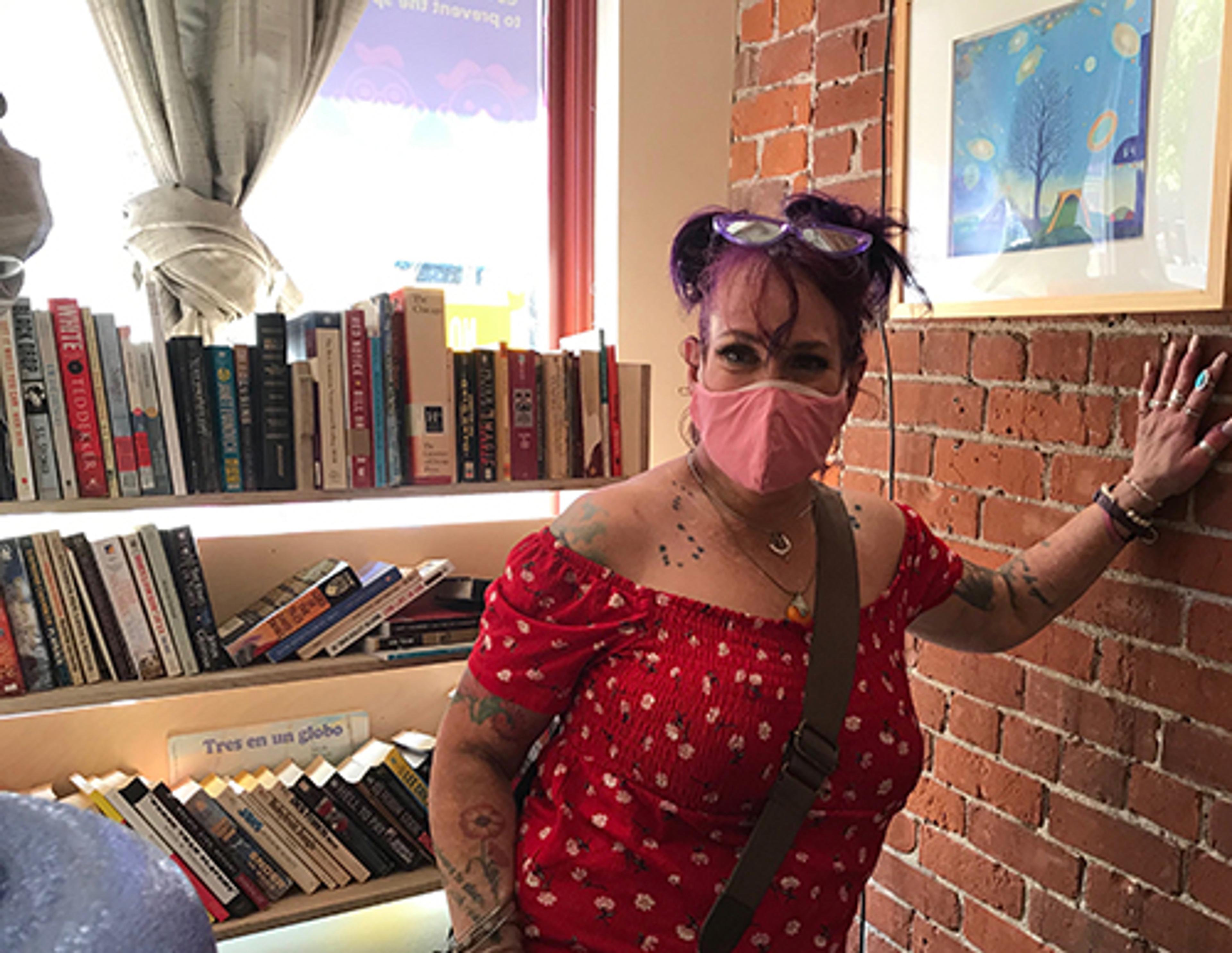 A woman in a mask with purple hair leans against wall