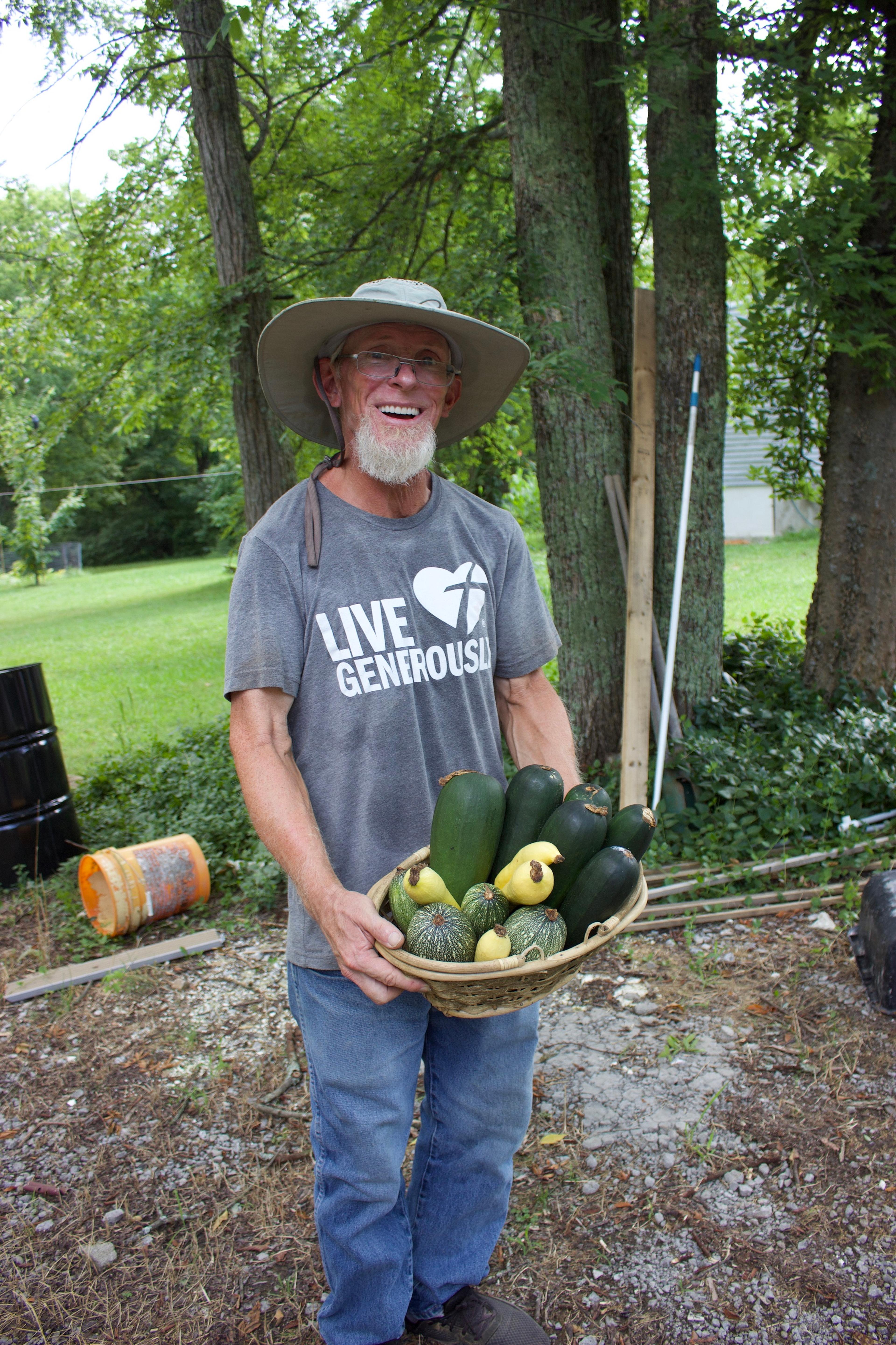 A bearded man in a hat holds vegetables in a basket