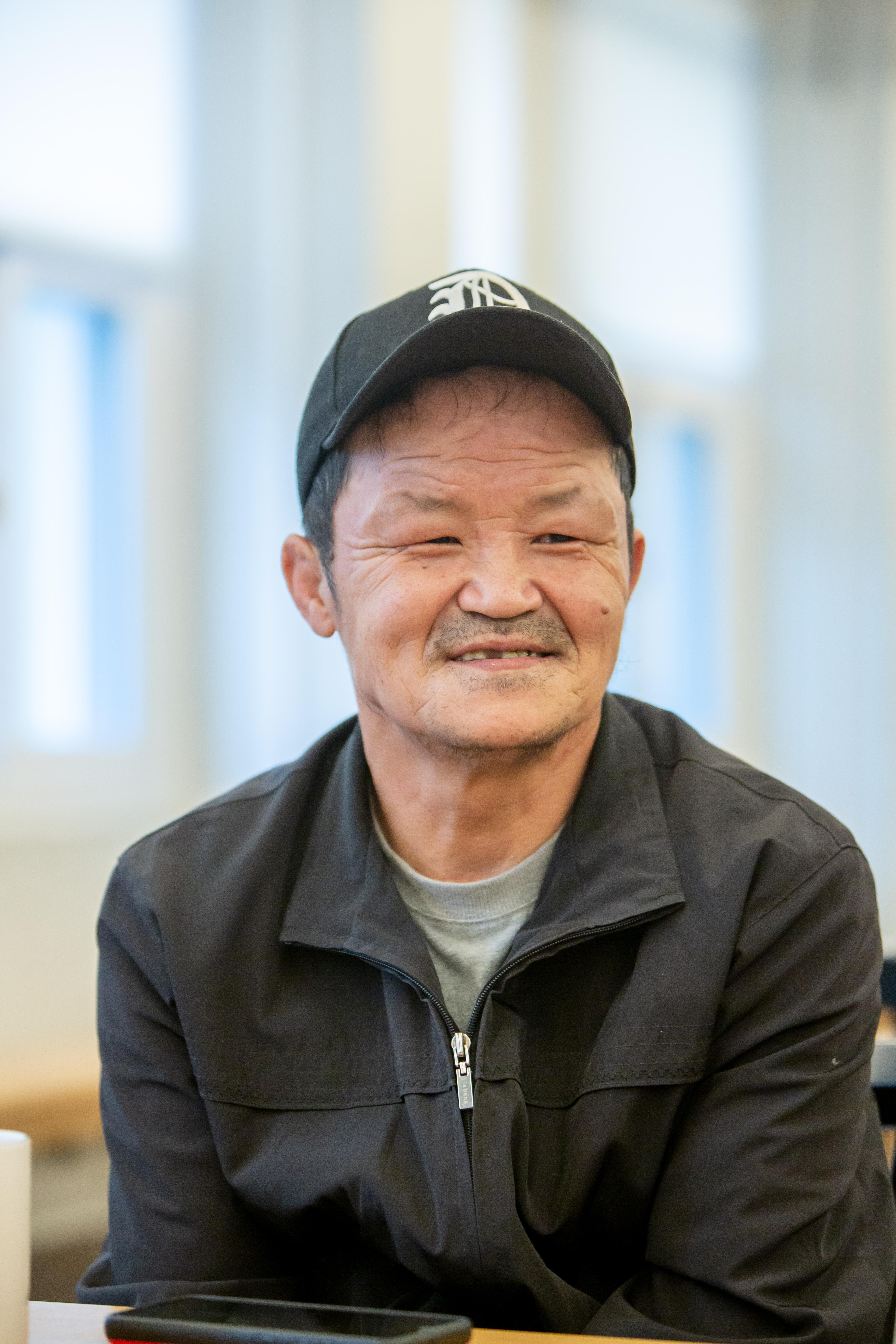 Big Issue Korea vendor Kwak Changgab faces the camera wearing a black cap and jacket.