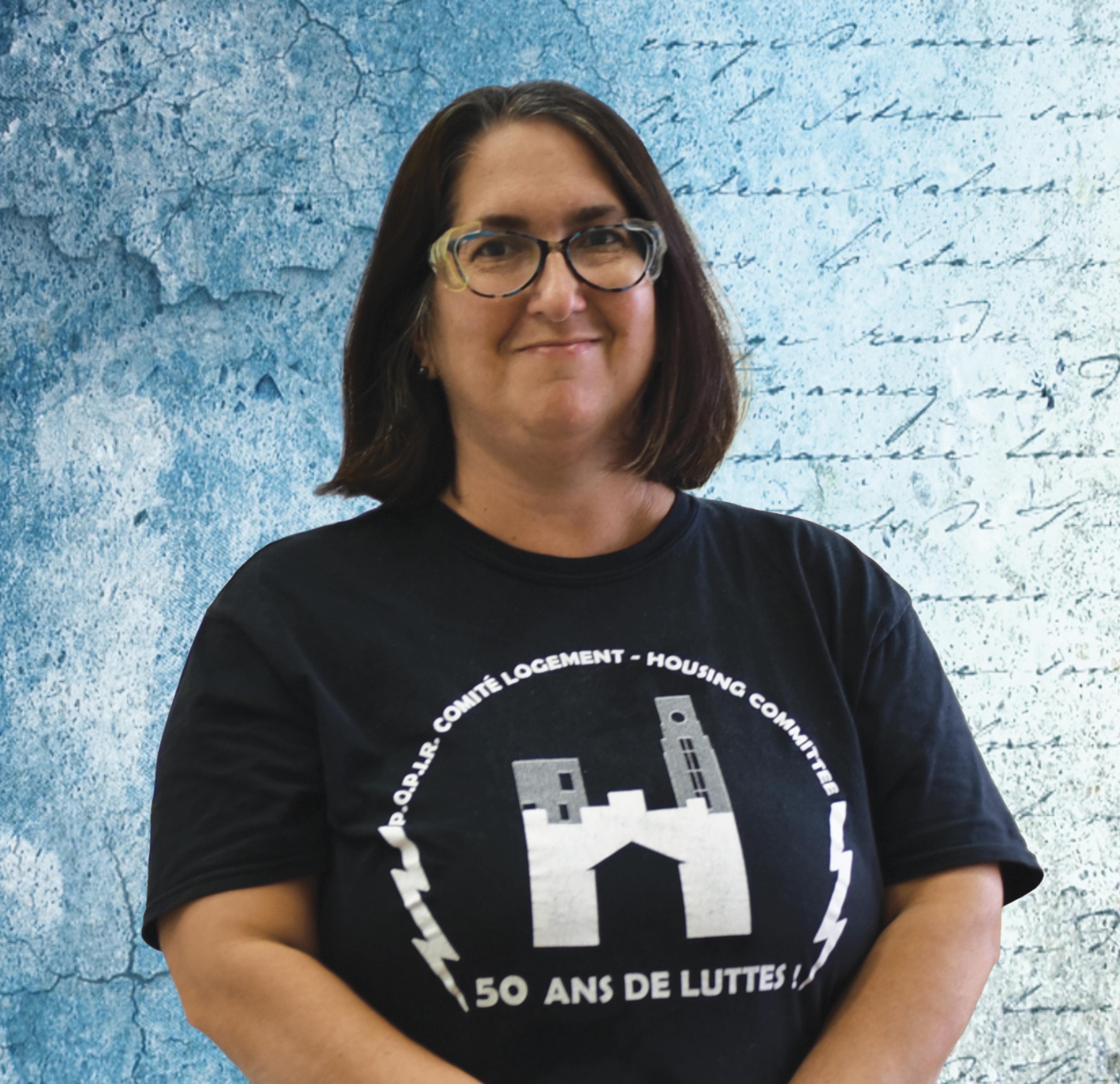 A woman in glasses stands in front of a background