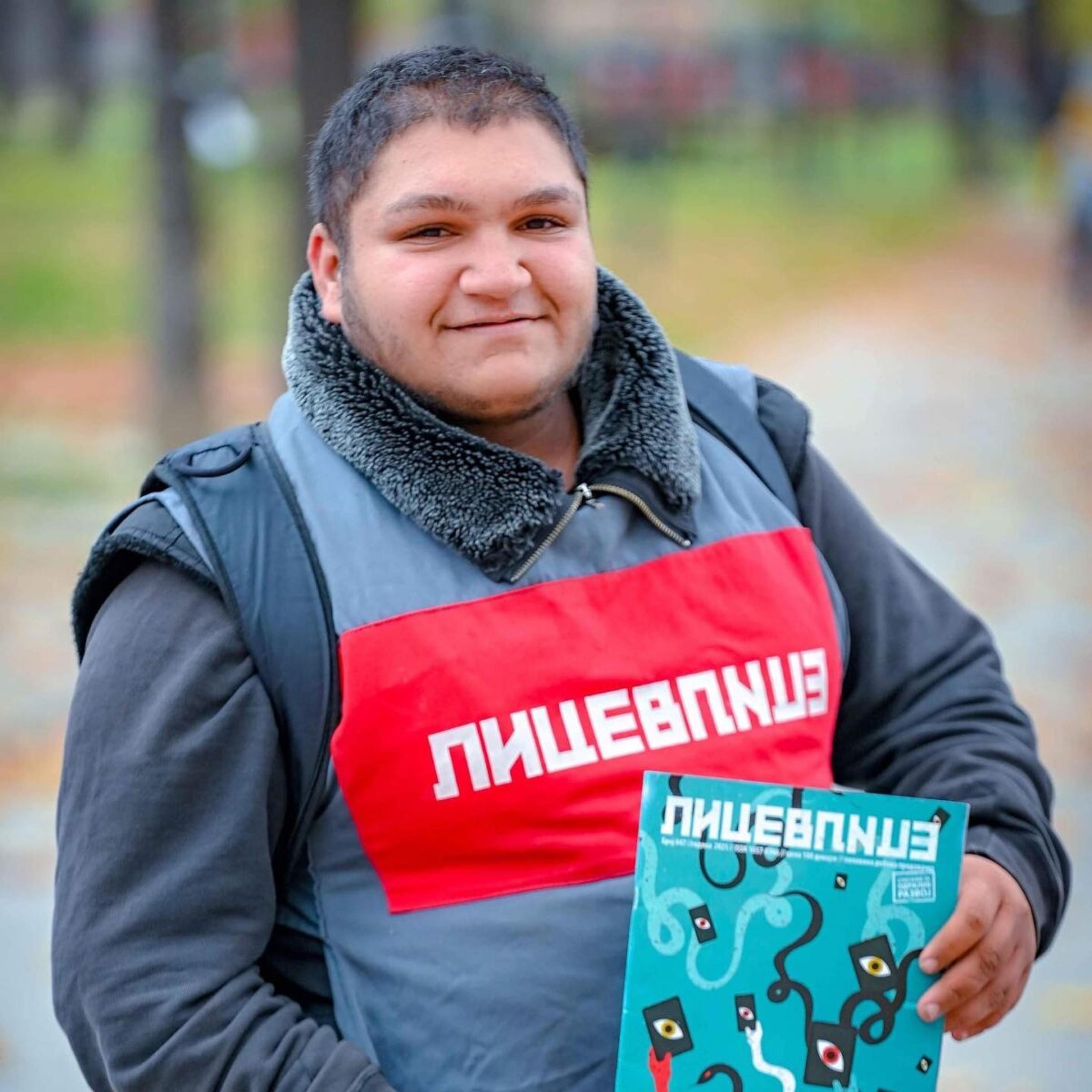 Lice v Lice vendor Memet Kamber, who passed away due to complications from diabetes, stands smiling holding a copy of the magazine, wearing a grey jacket and a red and grey vest.