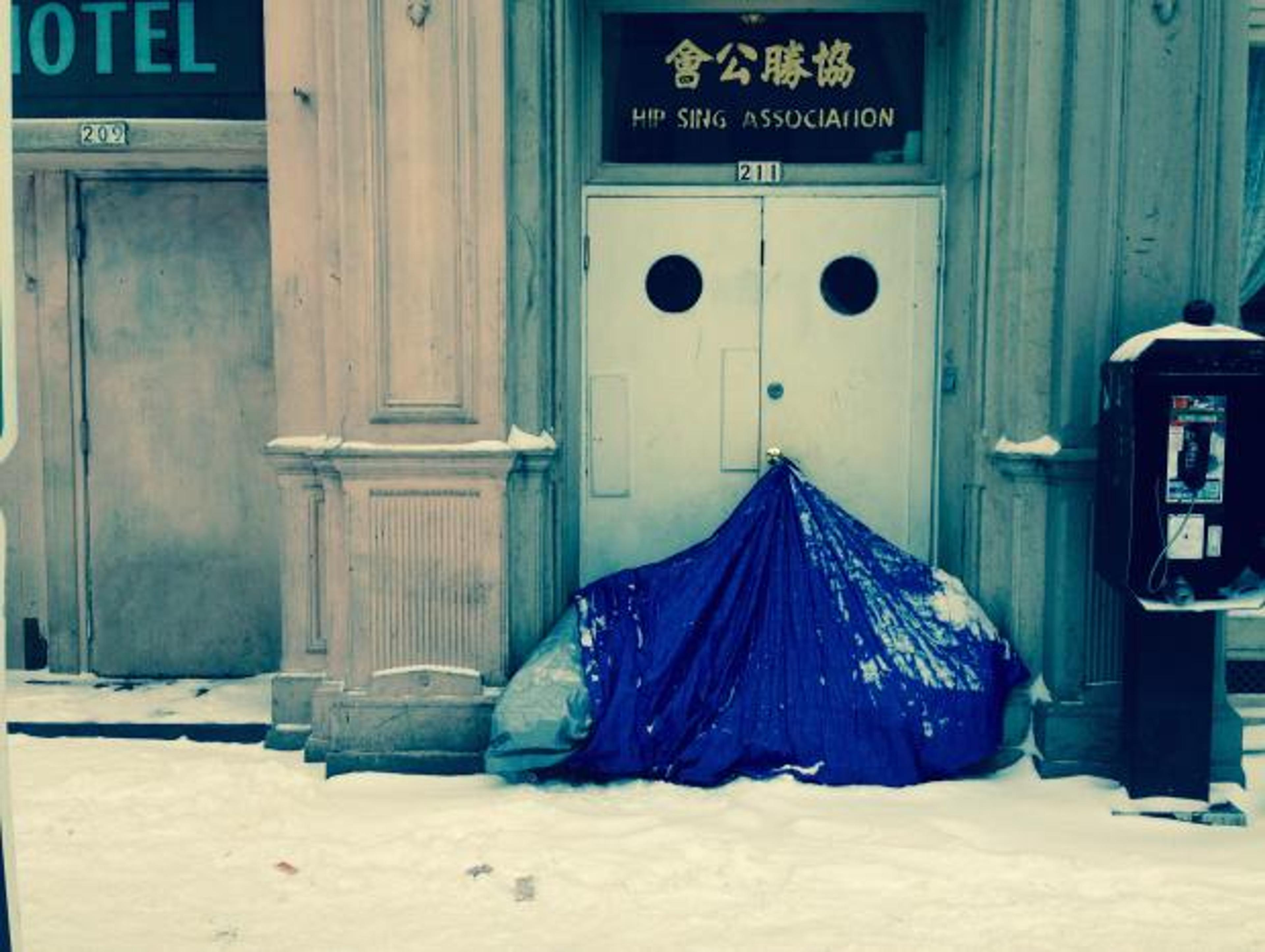 A homeless person sits in their tent on a snow covered street