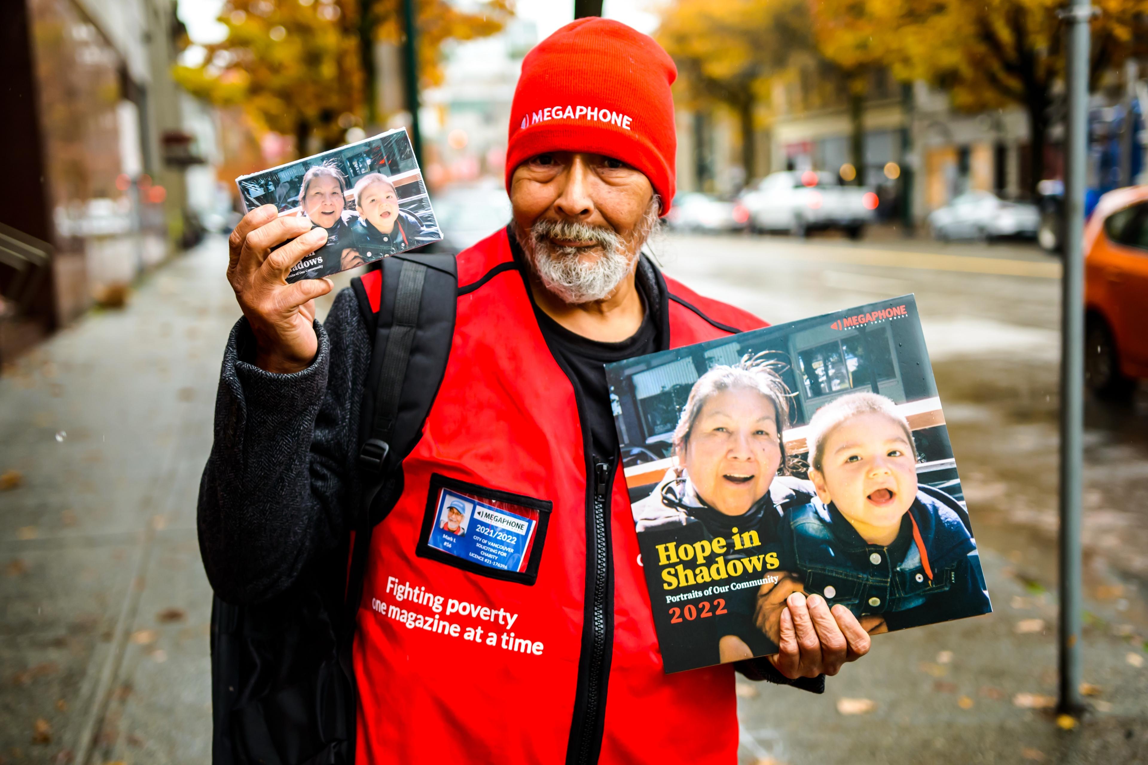 A man in a red hat and vest holding magazines and calendars