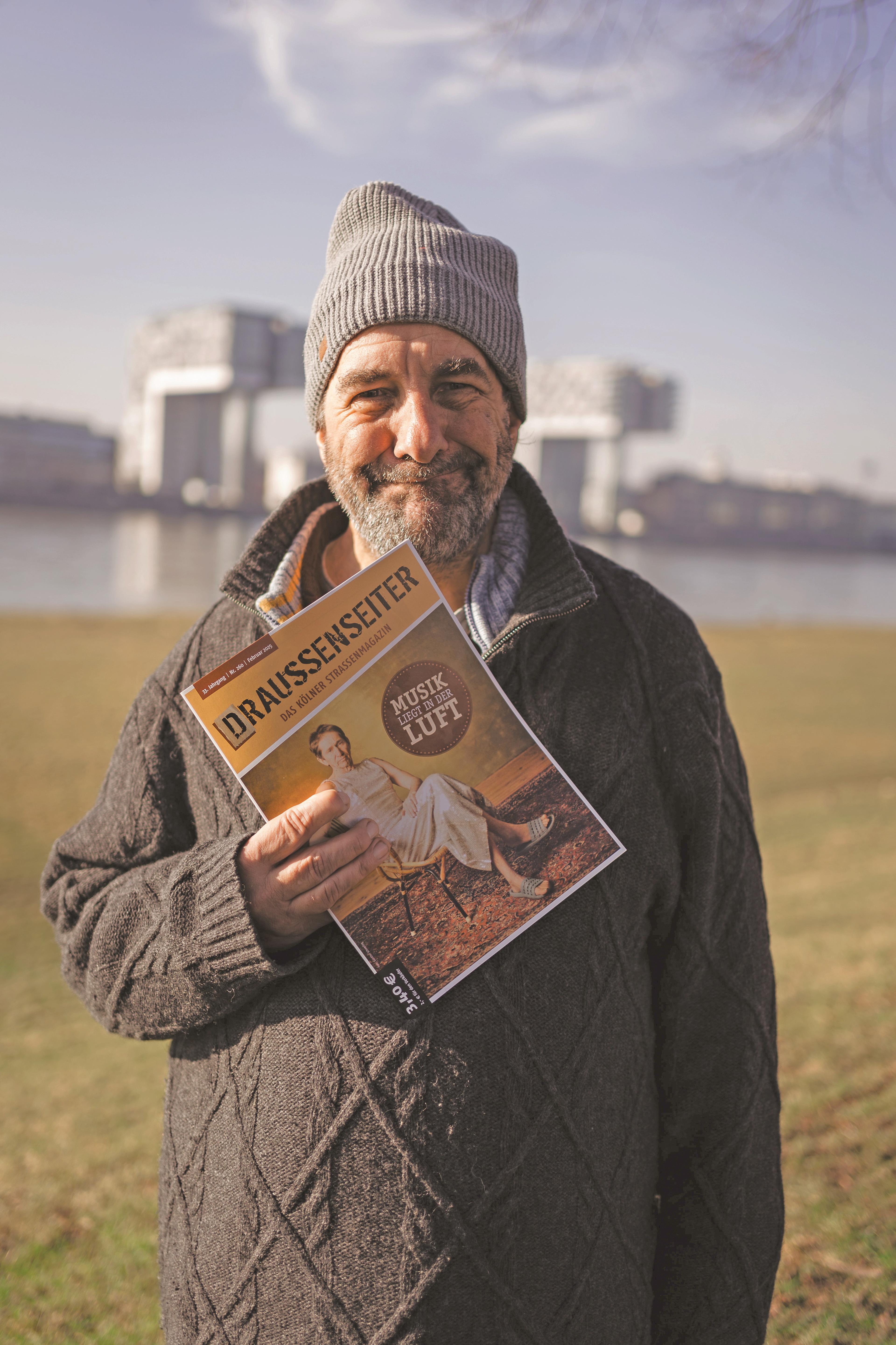 man in grey jacket standing with street paper and smiling
