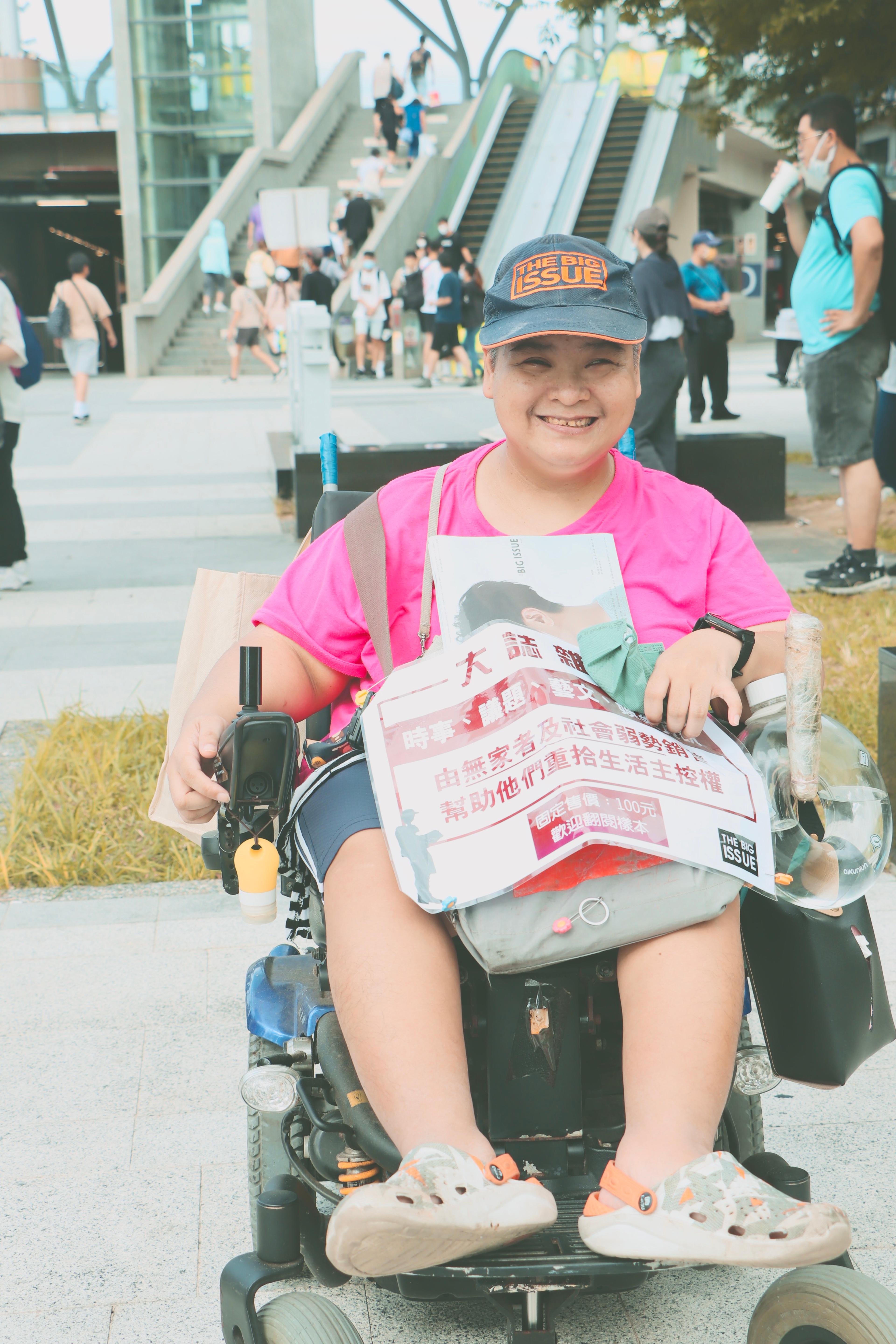 Hu Peilan smiles, wearing a cap, as she sits in her wheelchair selling The Big Issue Taiwan street paper