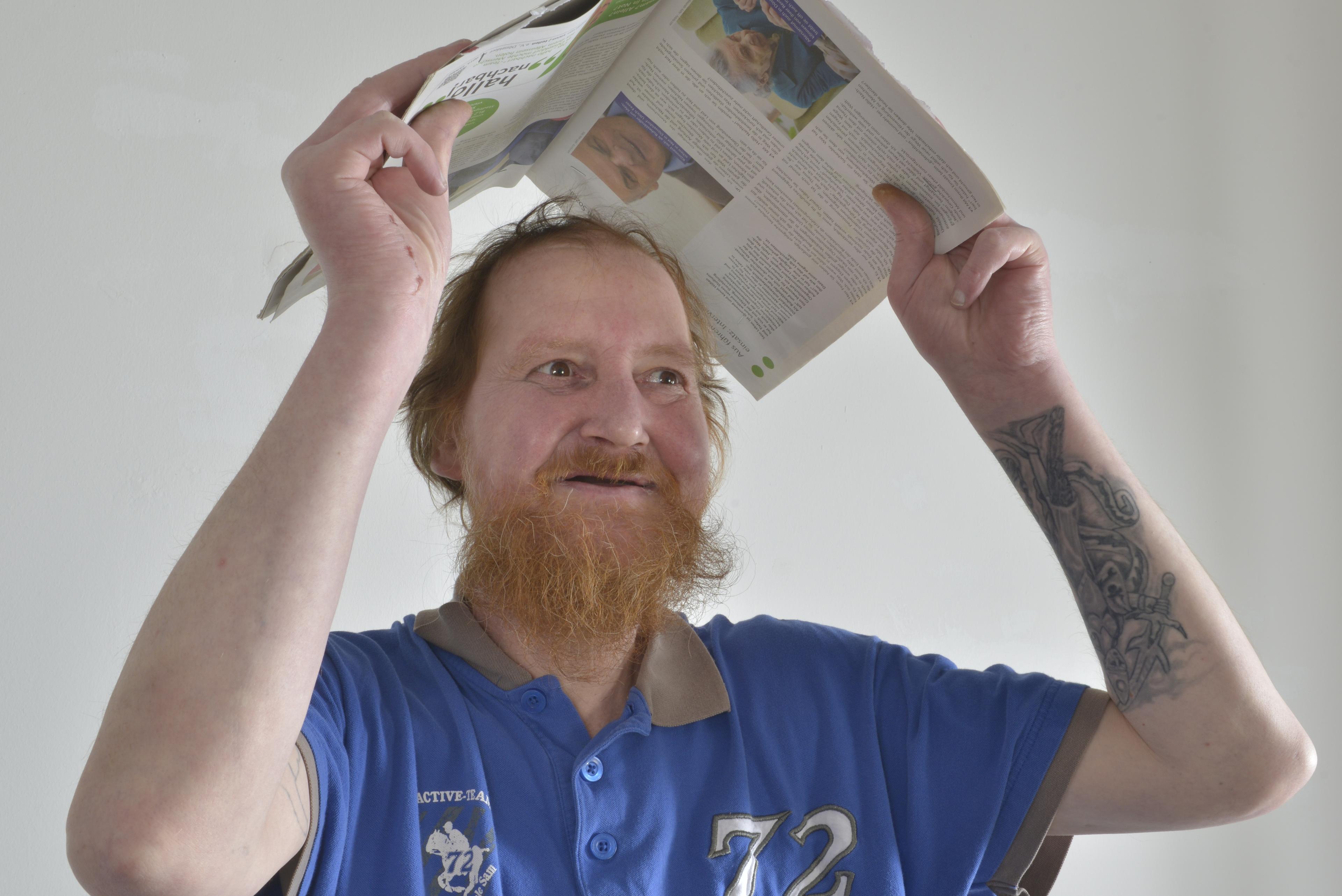 A man holds a newspaper over his head