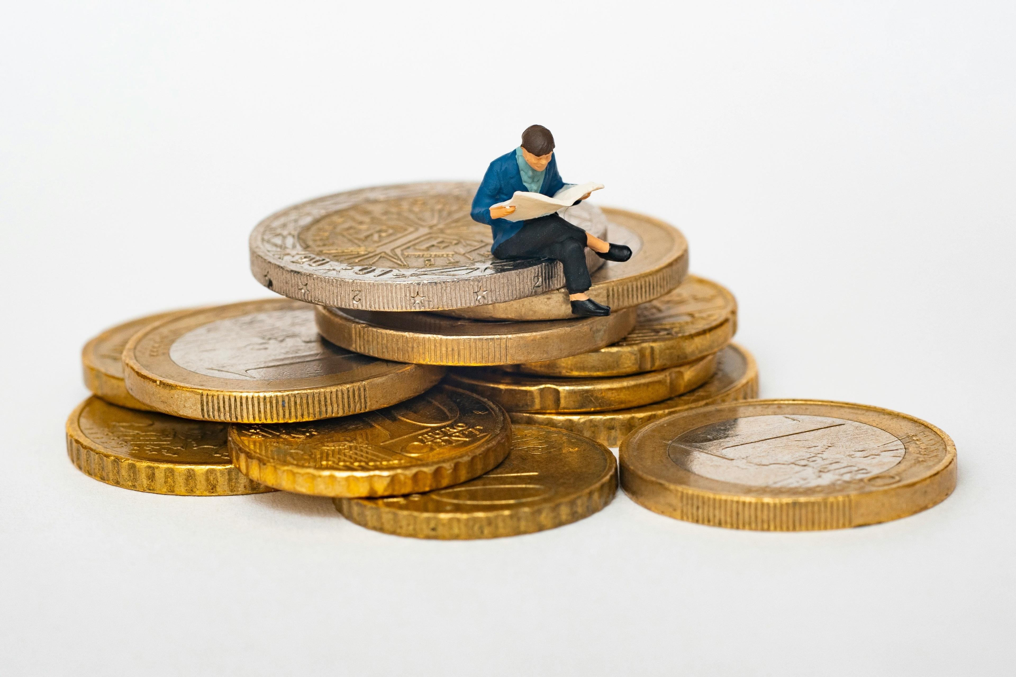 A model of a man reading a magazine sits on a pile of Euros.