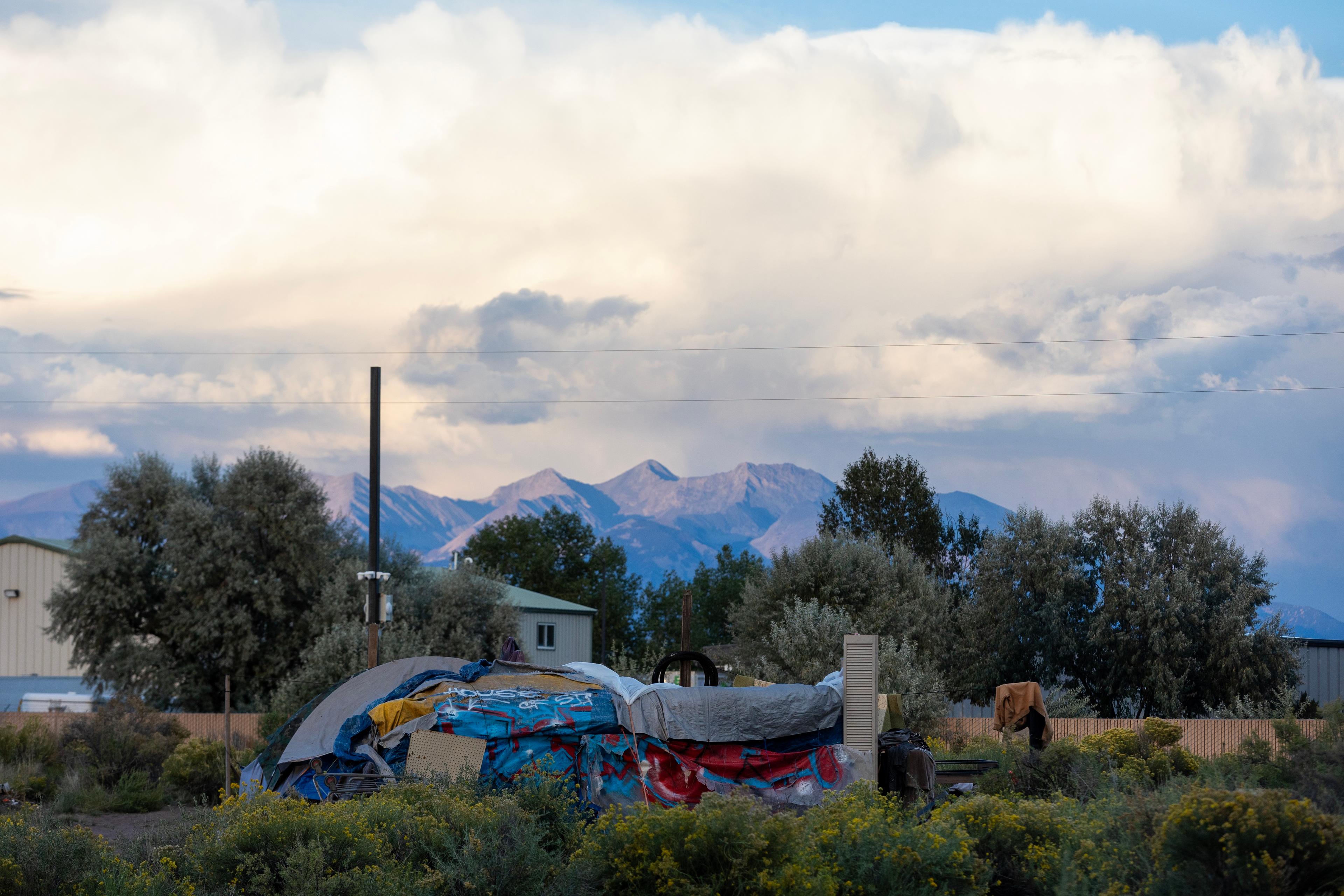 a pile of camping supplies sitting in a field, in front of houses and a mountain