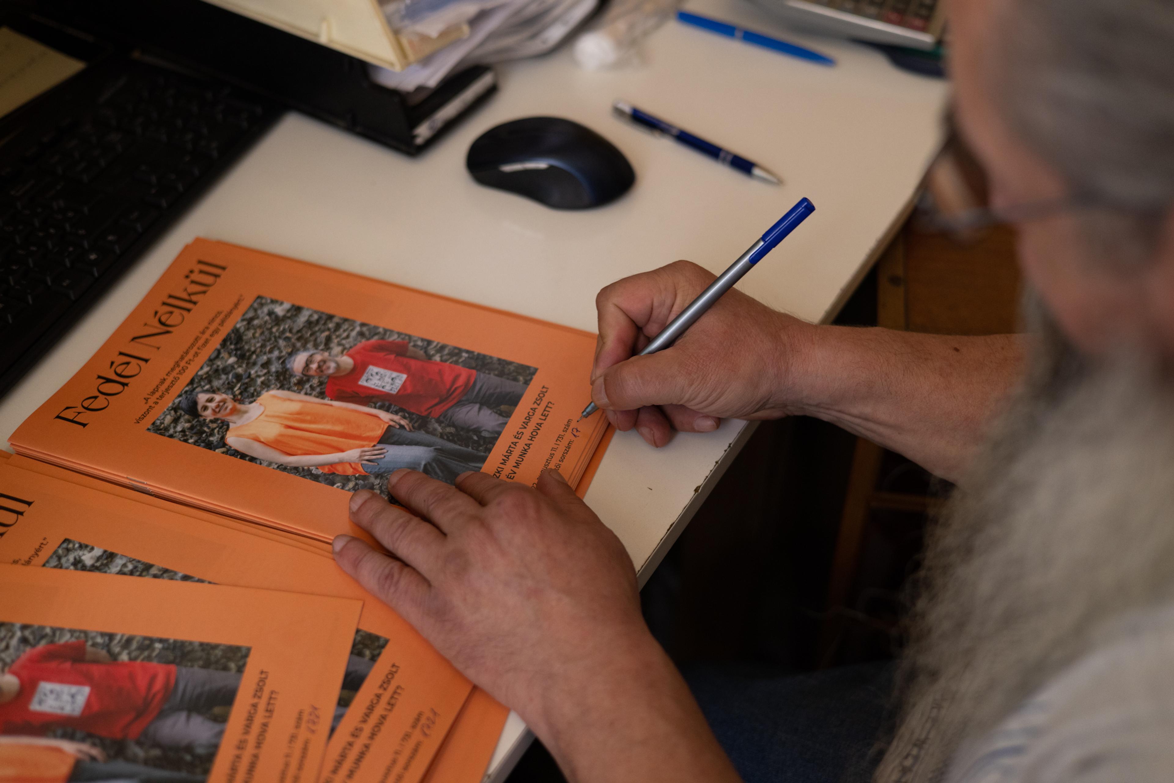 A street paper vendor writes their unique ID number on a recent issue of Fedél Nélkül