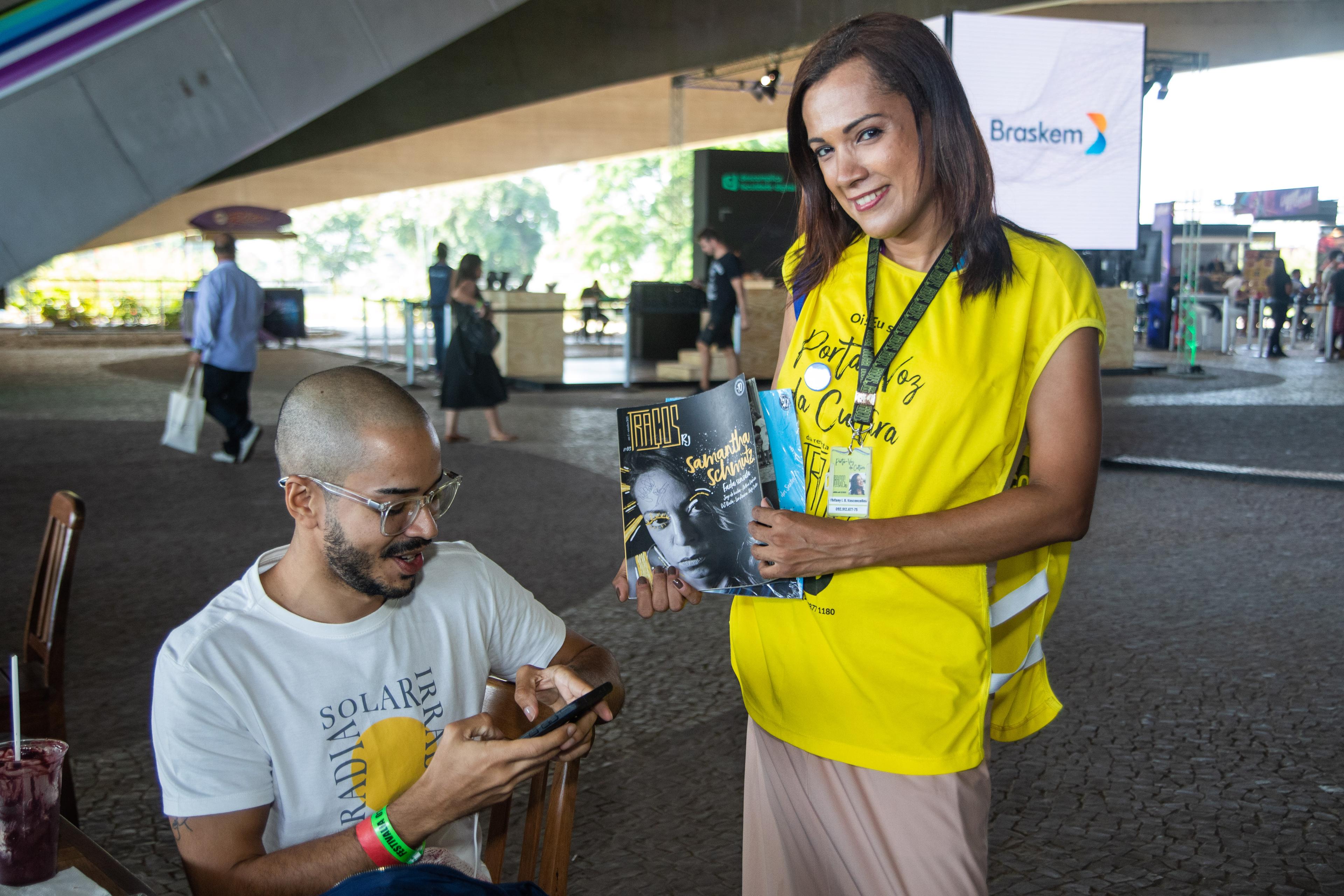 Tracos vendor Thifany, wearing her yellow vest and vendor badge, sells the magazine to a customer