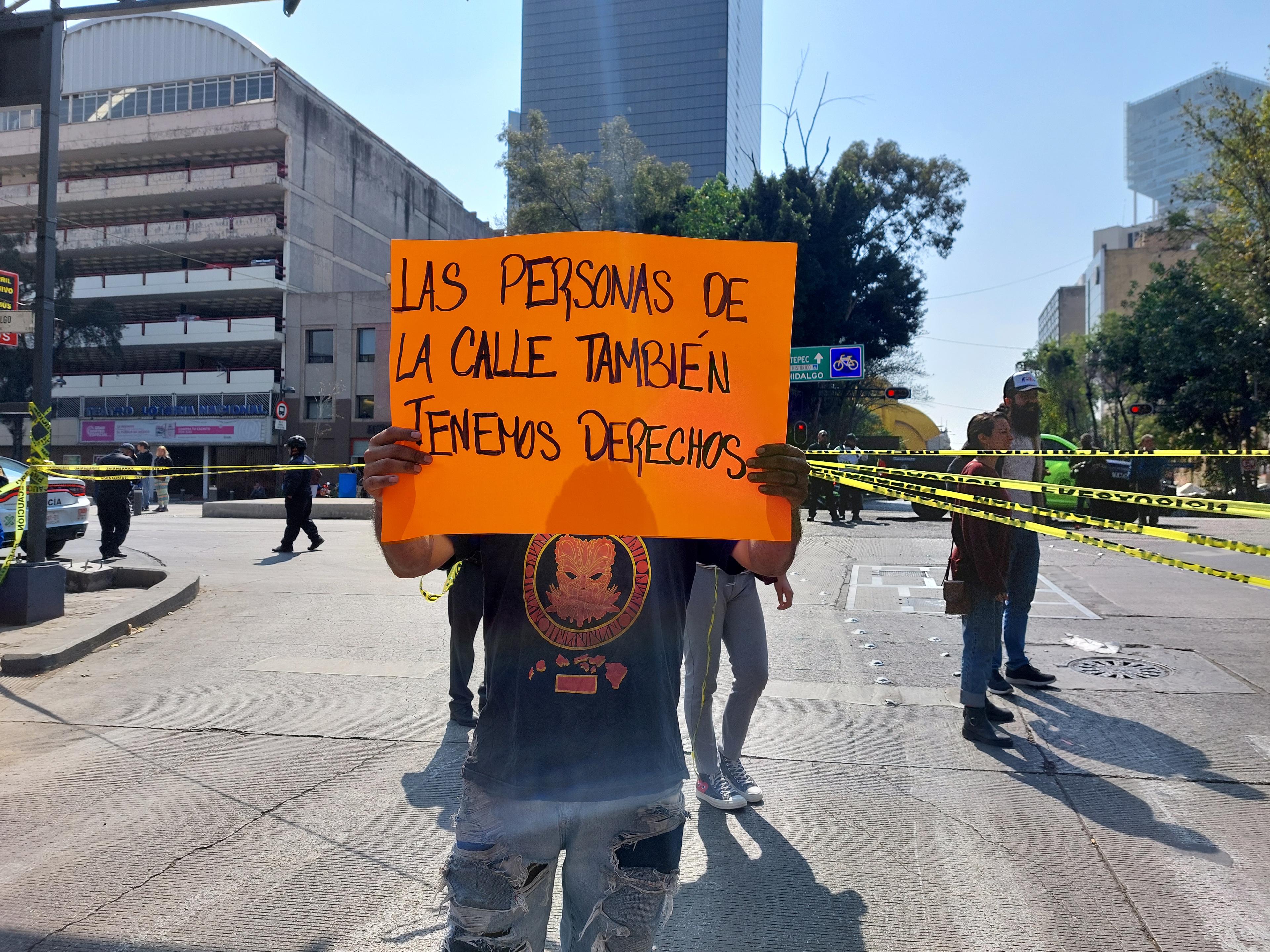 A protestor holds up a placard with a slogan in Spanish that translates roughly to "People on the streets have rights too"