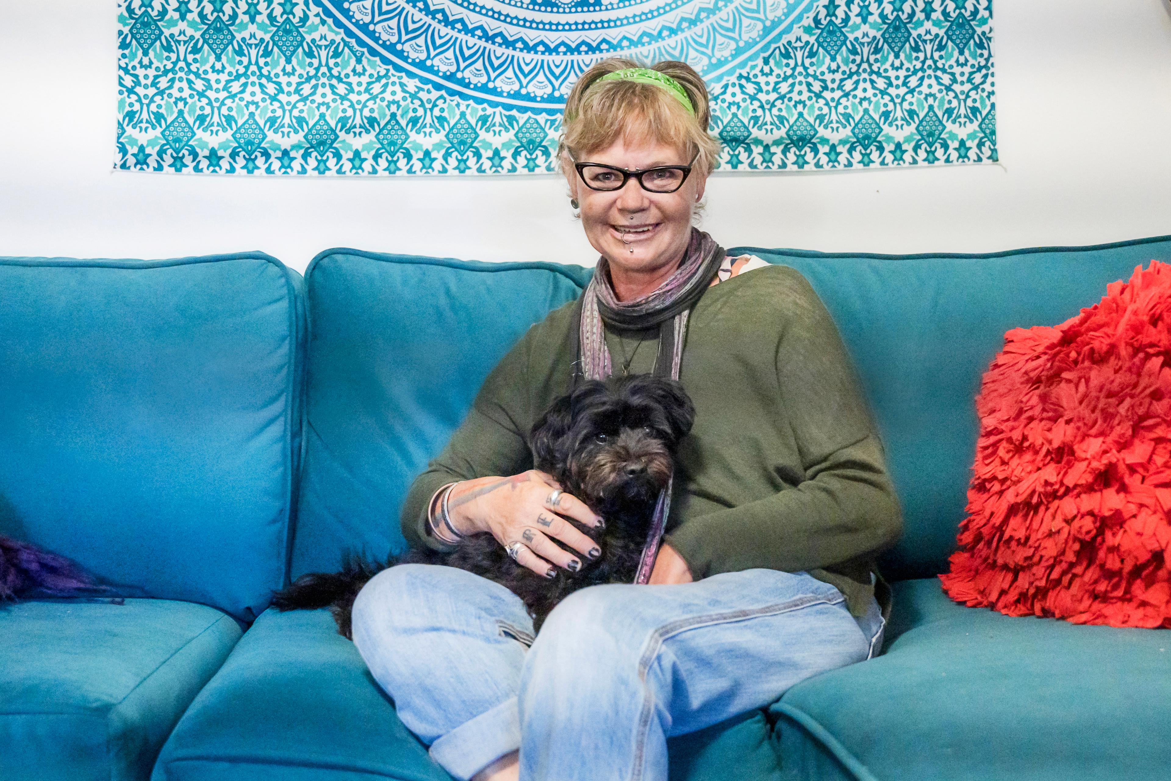 Danni sits on a blue sofa with her dog which has black fur,