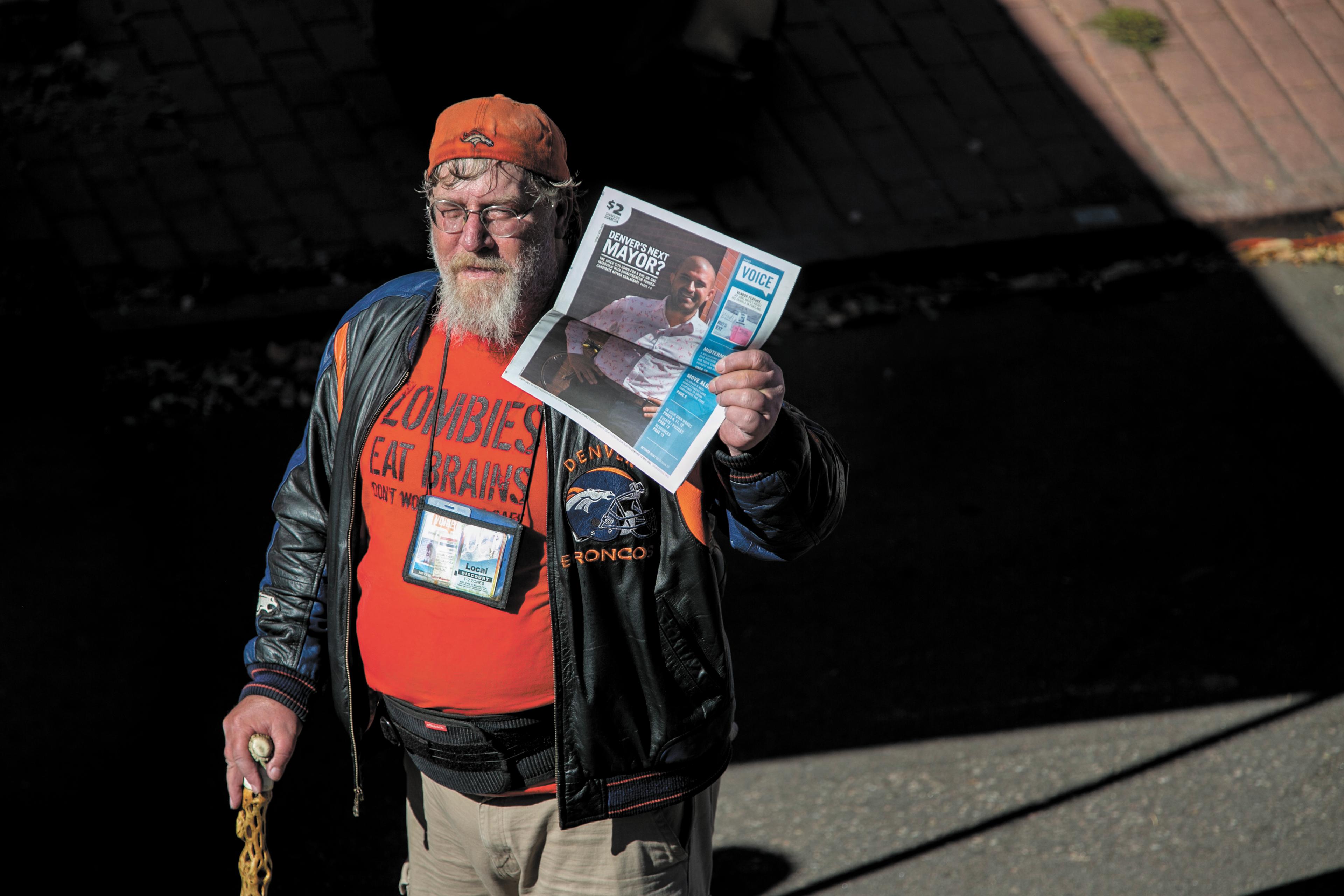 Man with a stick on the street holding a newspaper