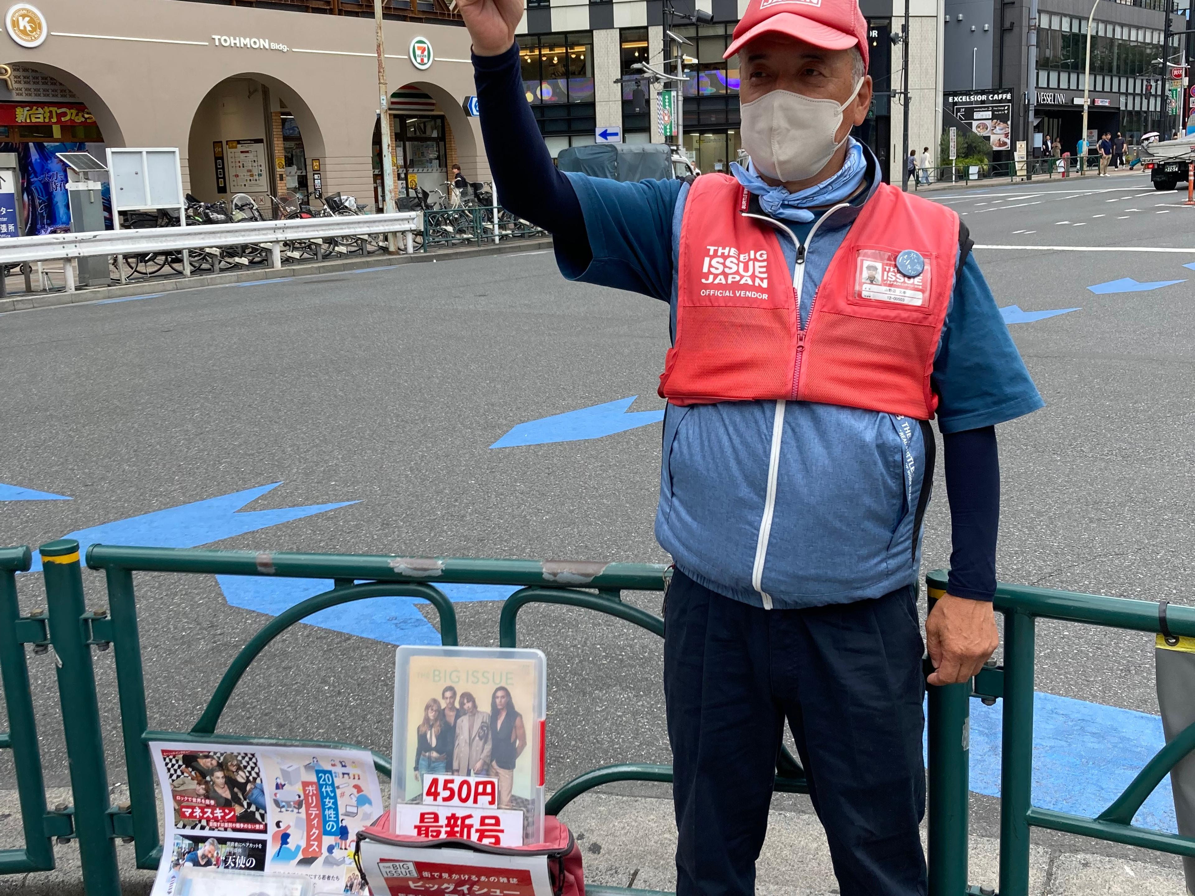 A Big Issue Japan vendor stands on the street in the heat wearing a jacket that regulates air to cool the wearer down.