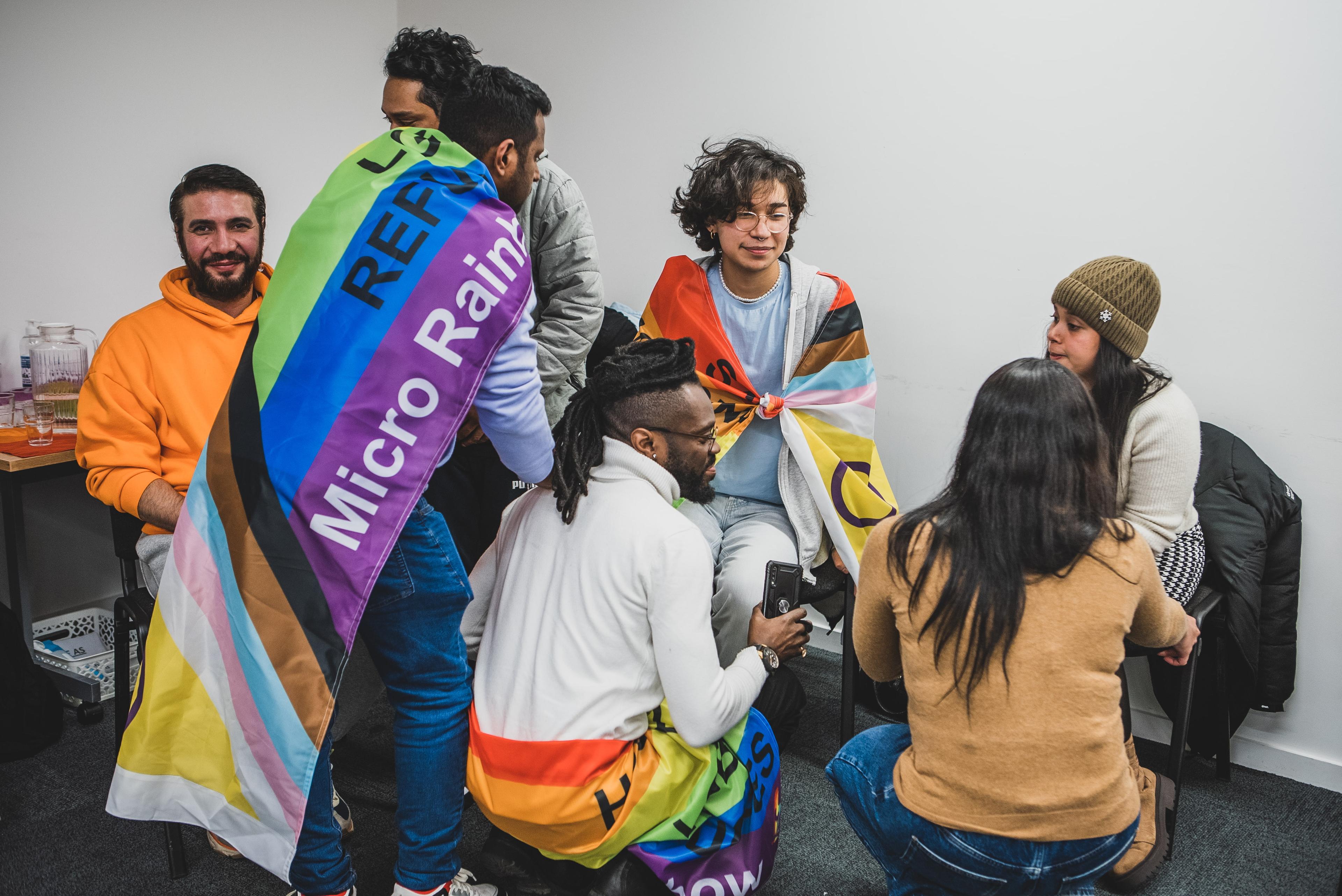 group of people chatting with Pride flags wrapped around their shoulders