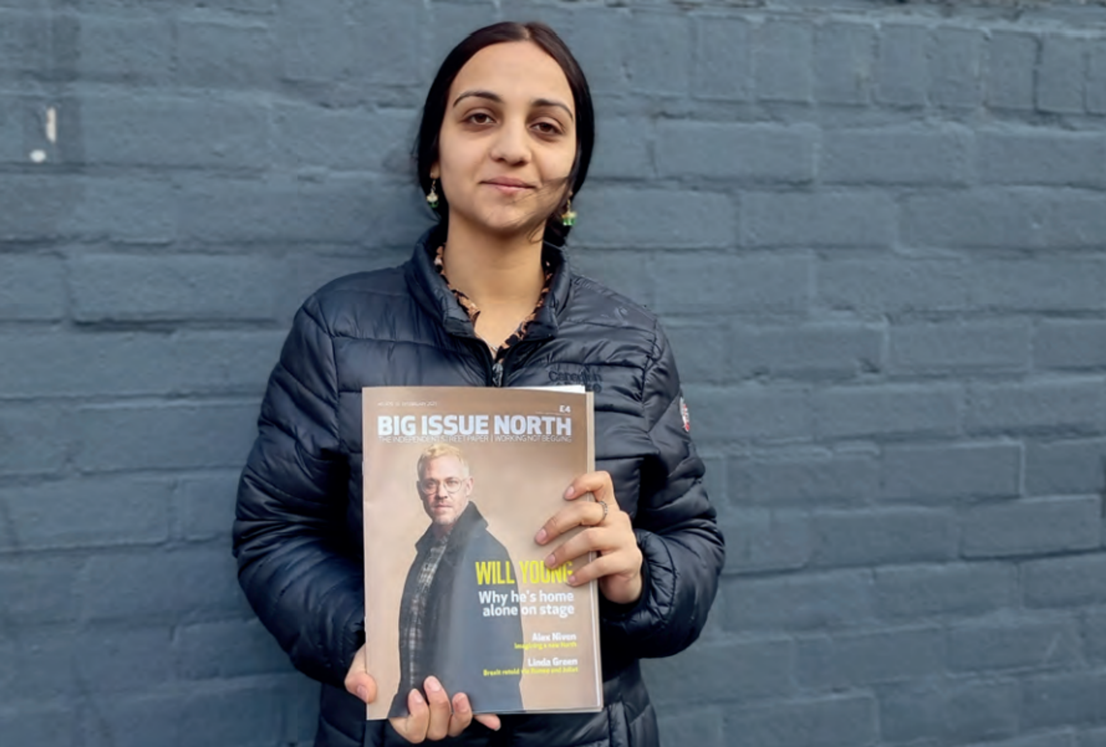 Sara, who sold the Big Issue North in Southport, stands with the magazine against a black brick wall