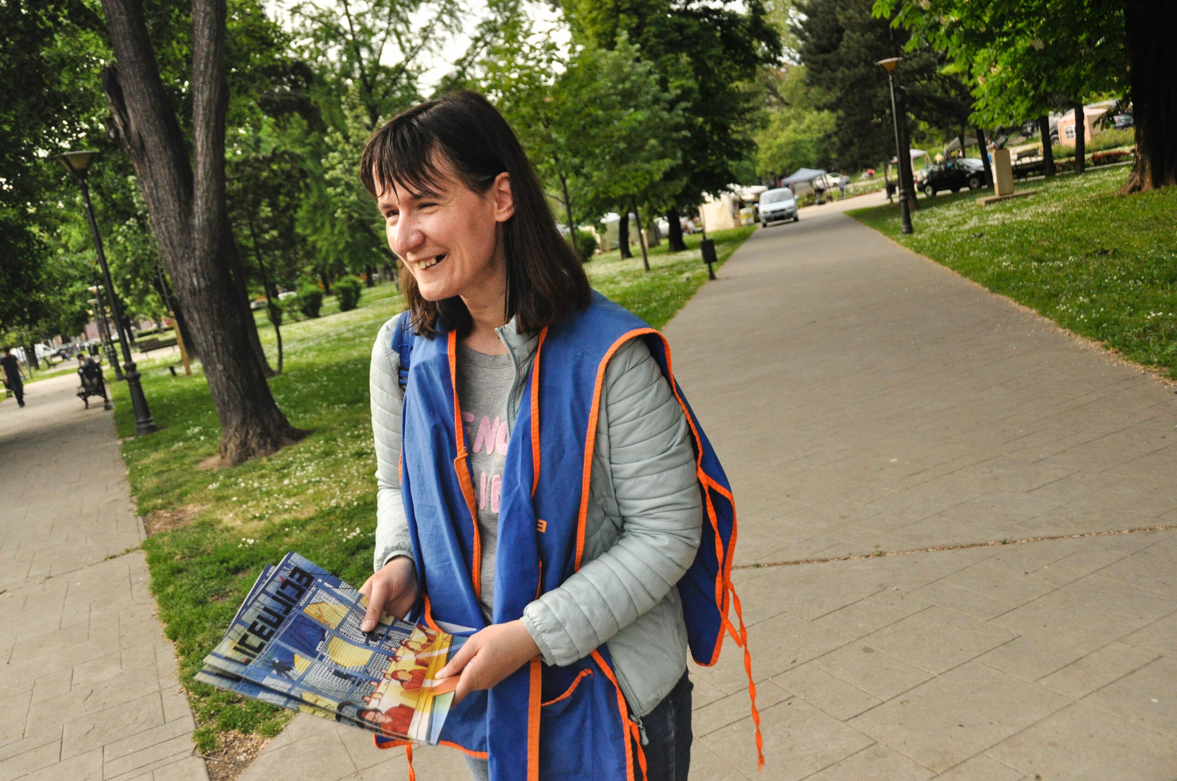 A woman in a blue vest sells the Serbian street paper Liceulice