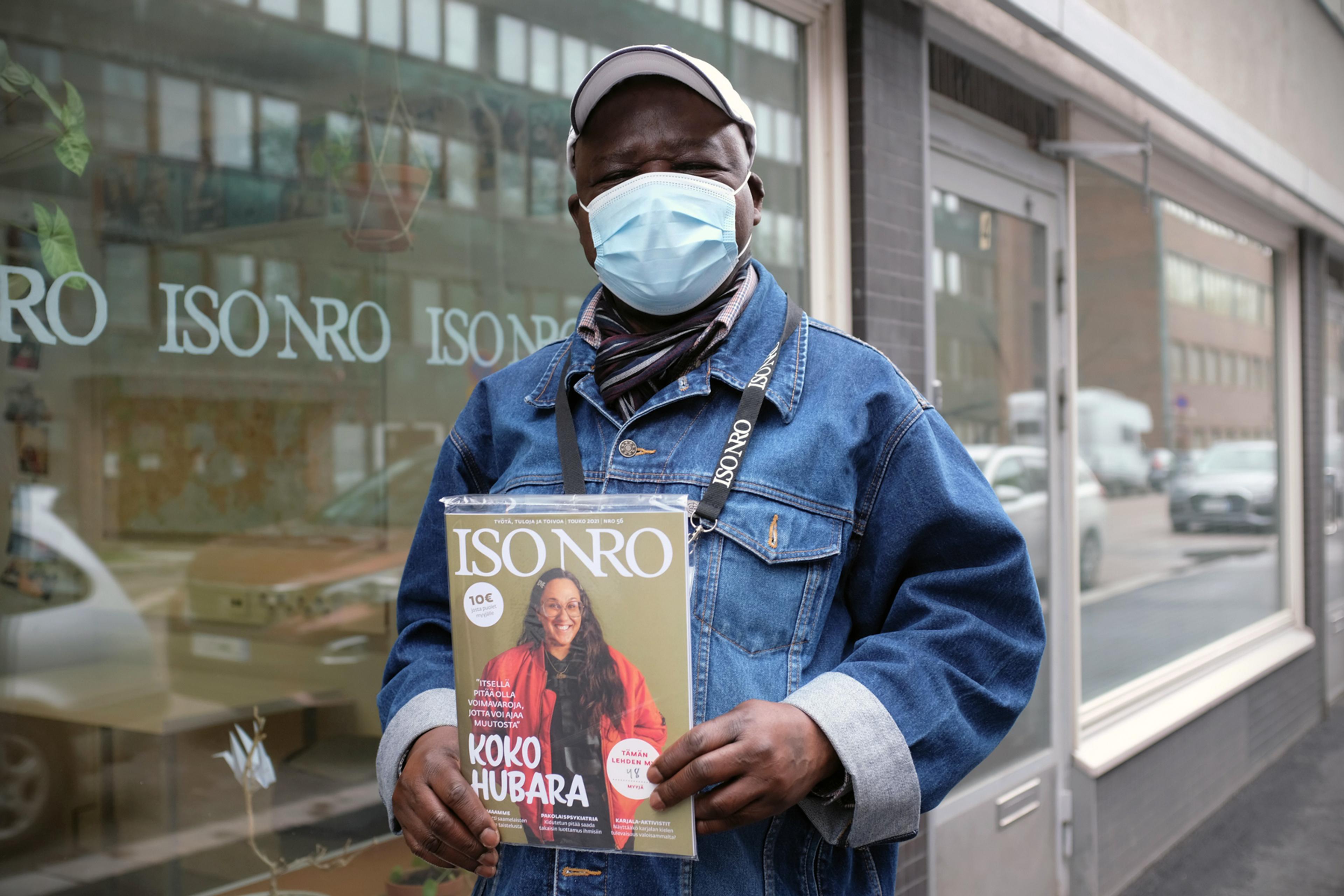 Street paper vendor wearing a mask and holding a copy of Iso Numero