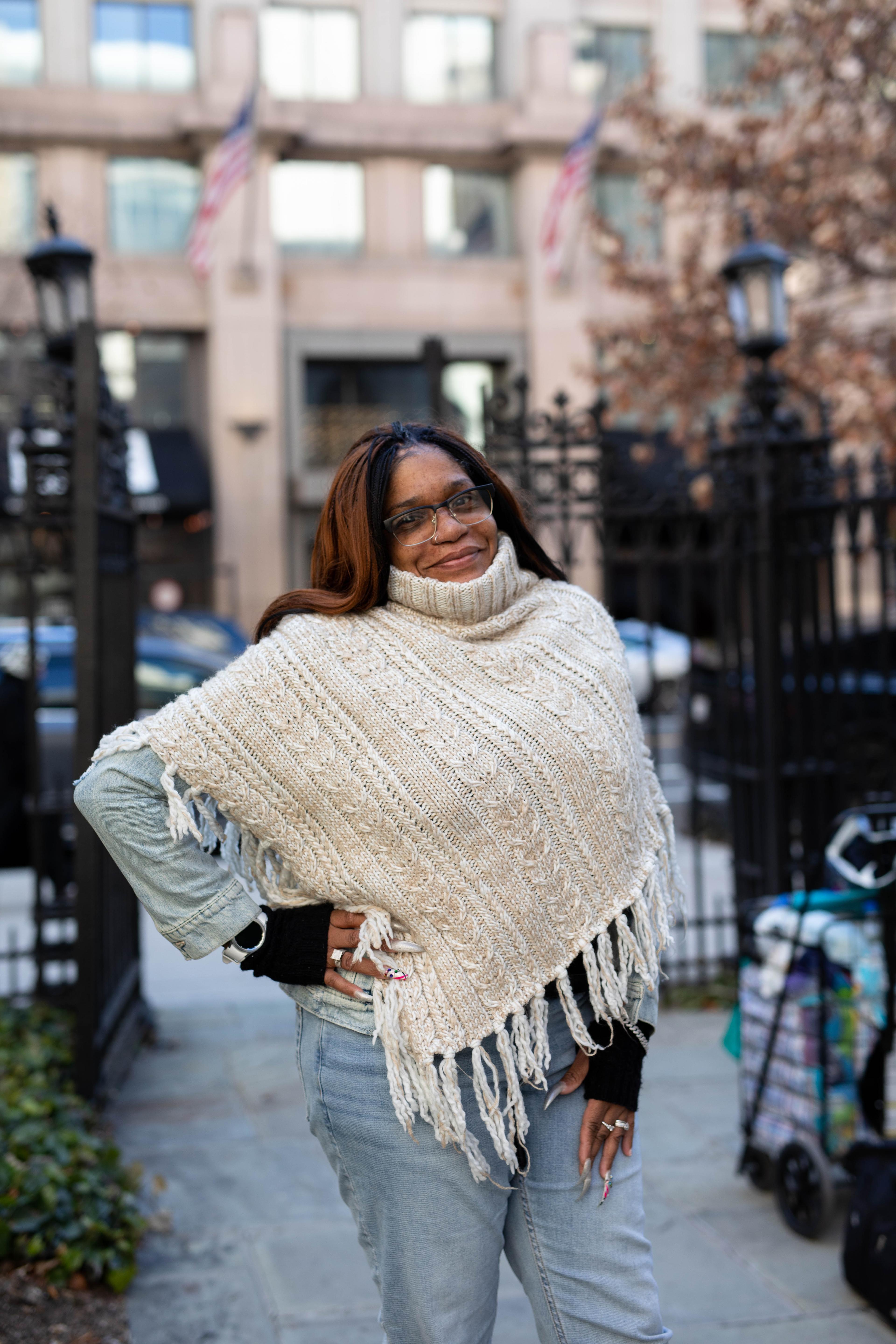 a woman in a white poncho stand smiling with hand on hip