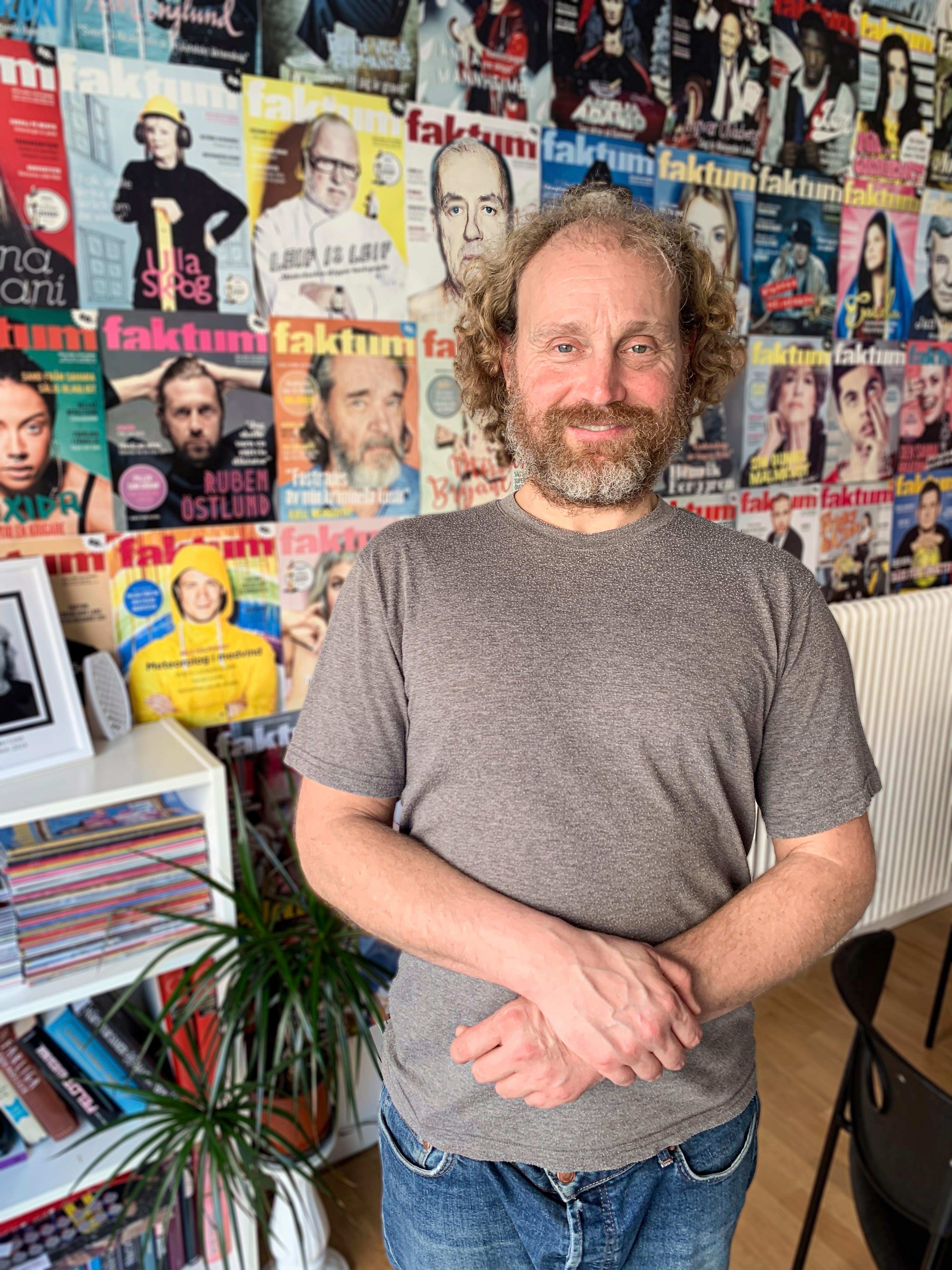 a man in a grey t-shirt standing in foront of a rack of magazines