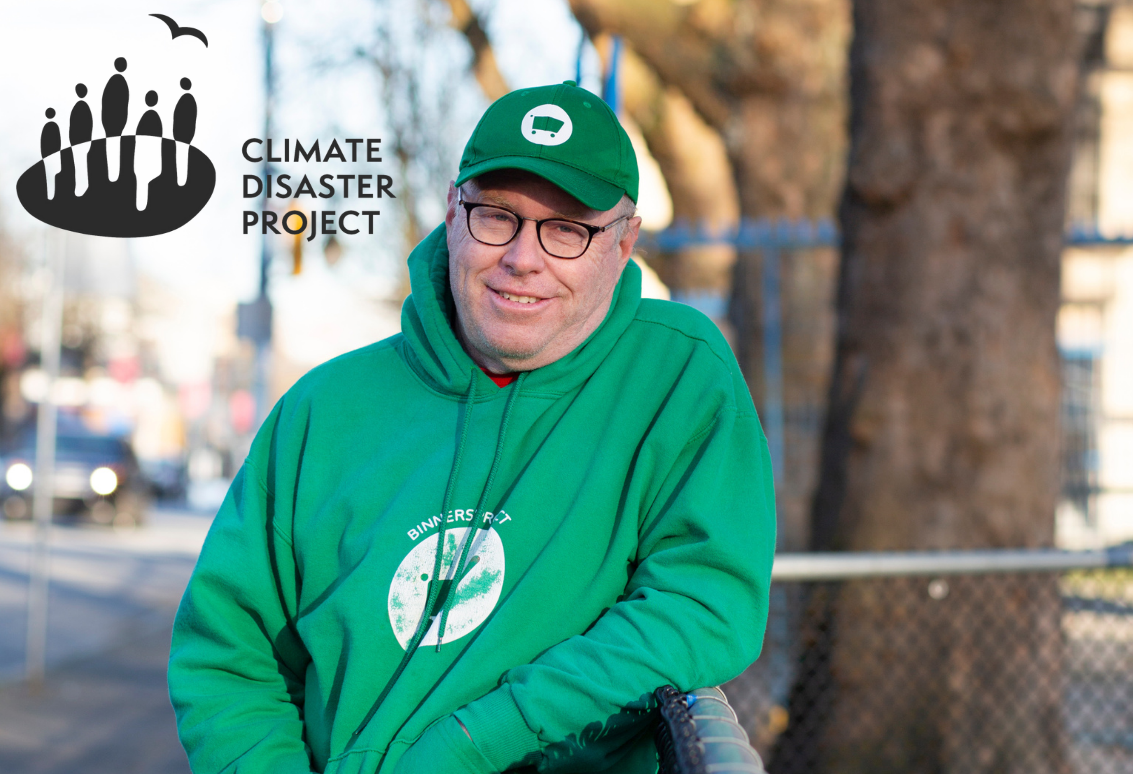 Mike McNeely leans against a fence in a green hat and hoodie